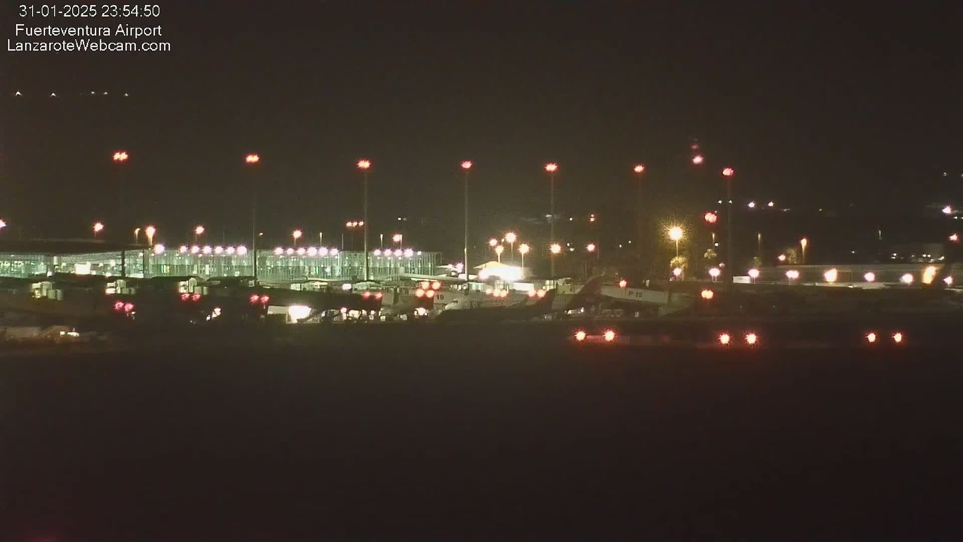 A nighttime view of an airport tarmac with several airplanes and illuminated airport buildings.