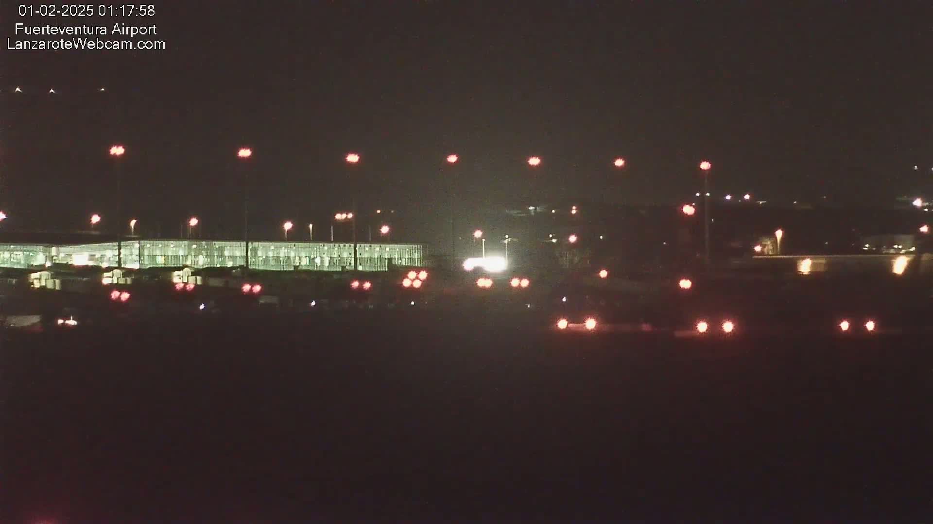 A nighttime view of an airport terminal building illuminated, with runway lights visible in the foreground and background under a clear, dark sky.
