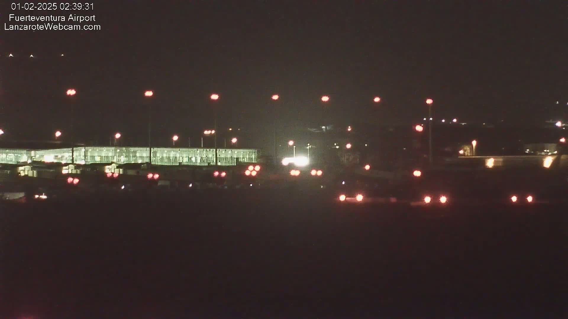 A nighttime long shot of an airport terminal building with various lights illuminating the scene under a dark sky.