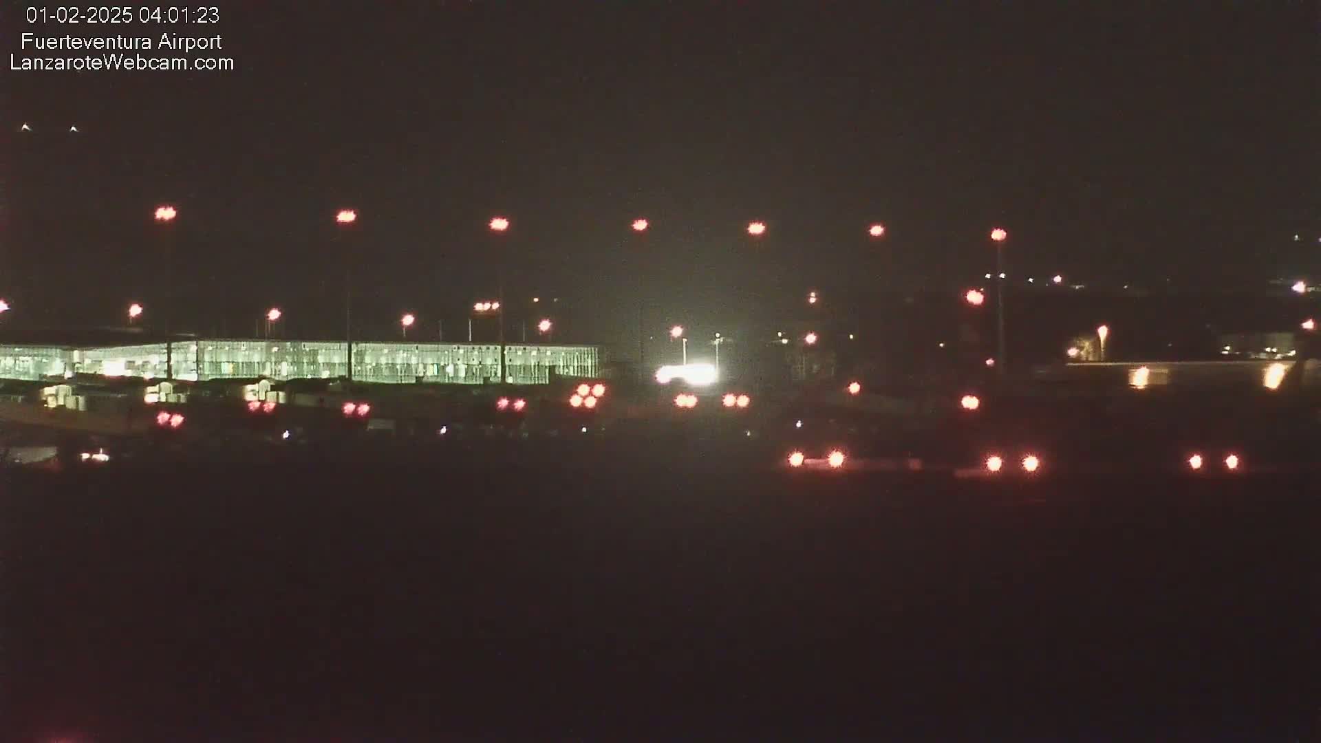 A nighttime view of an airport terminal with numerous lights illuminating the tarmac and runway.