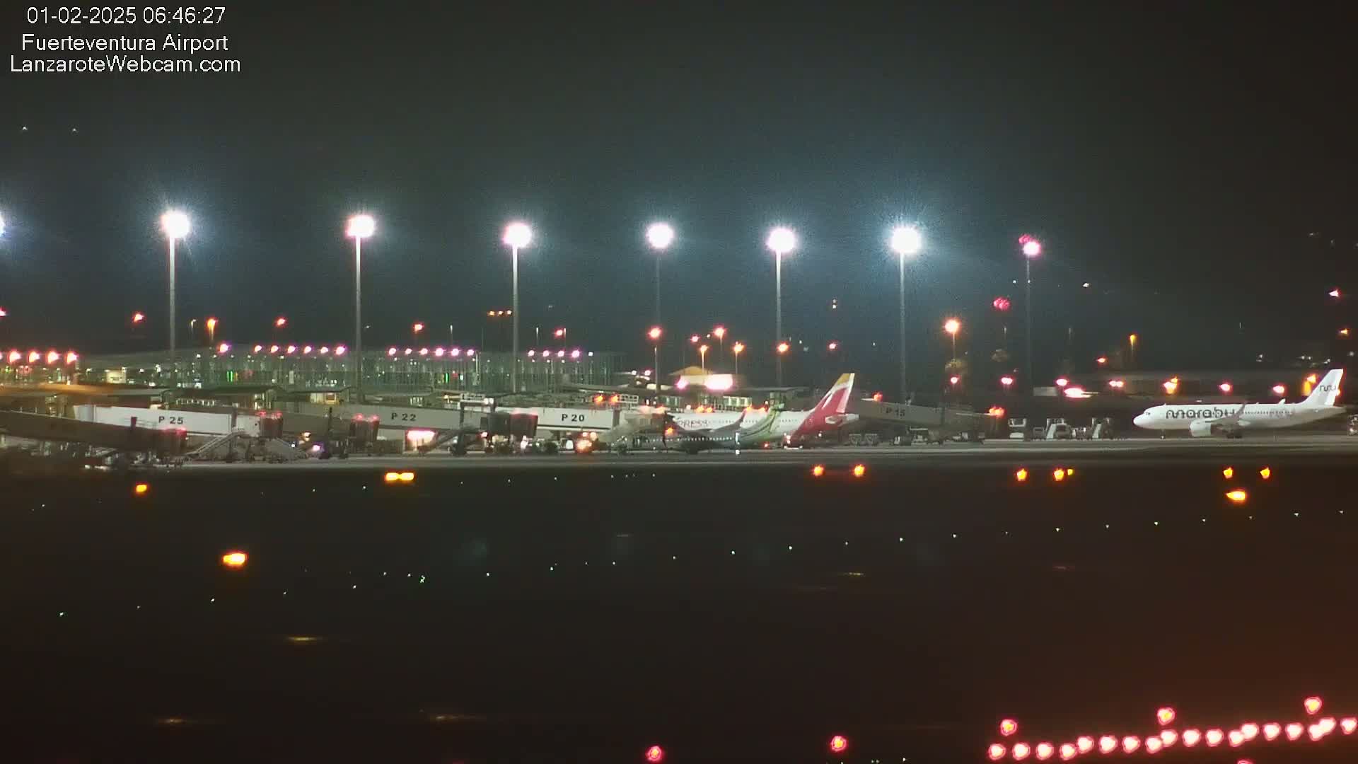 Several airplanes are parked at night at a brightly lit airport terminal.