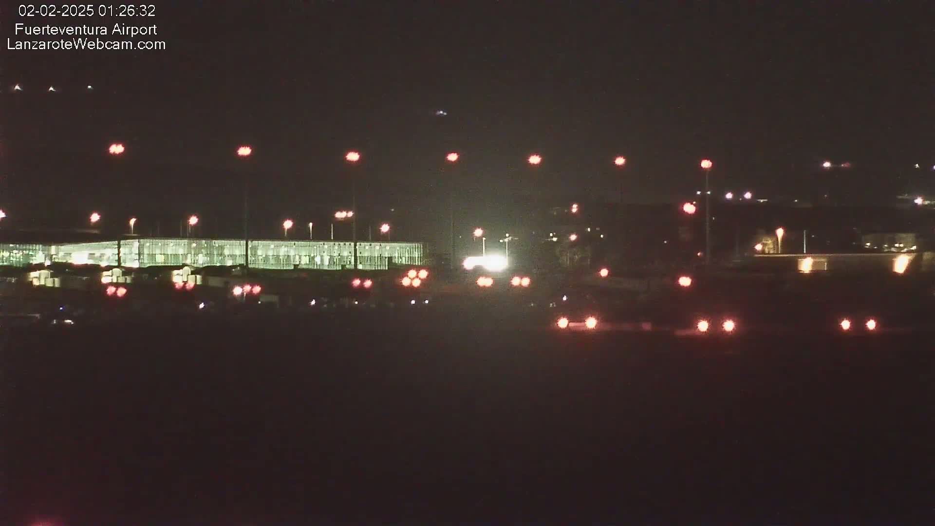 A nighttime view of an airport terminal building and tarmac, illuminated by numerous lights.