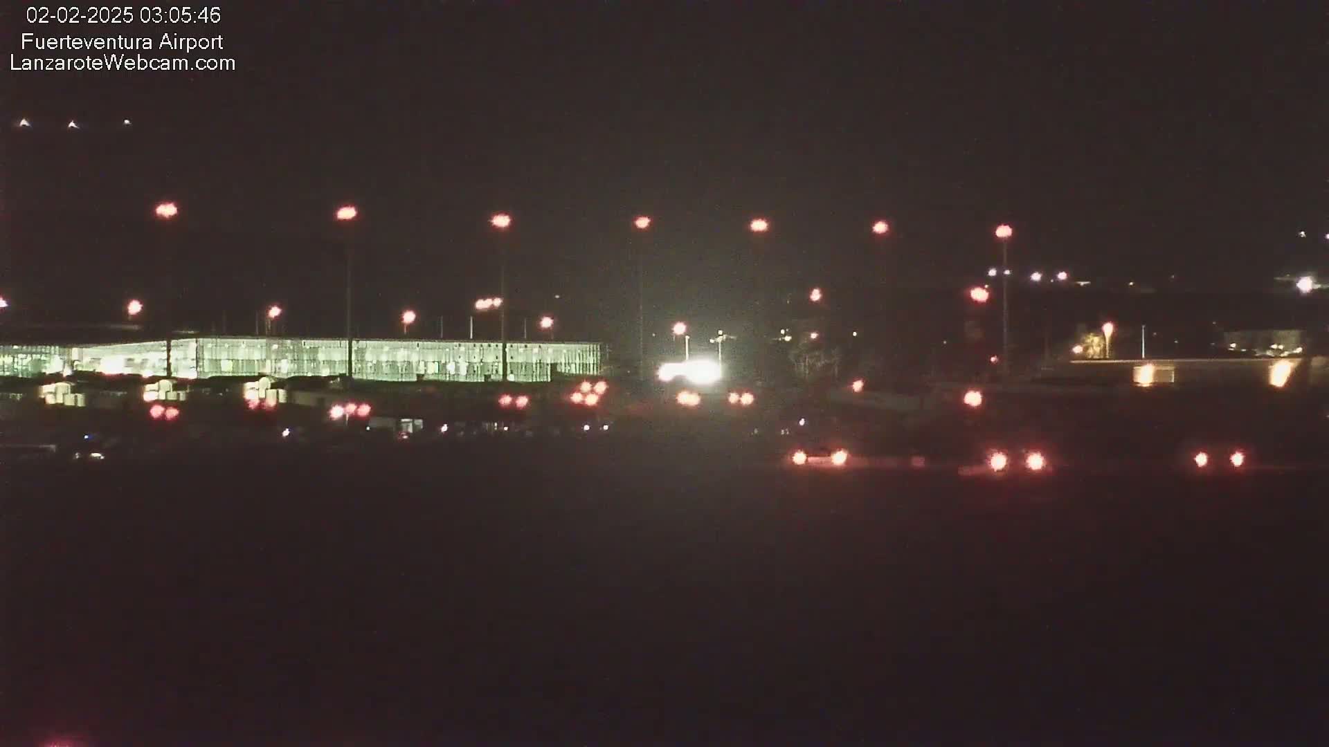 A nighttime view of an airport terminal building illuminated by lights, with vehicles visible on the tarmac.