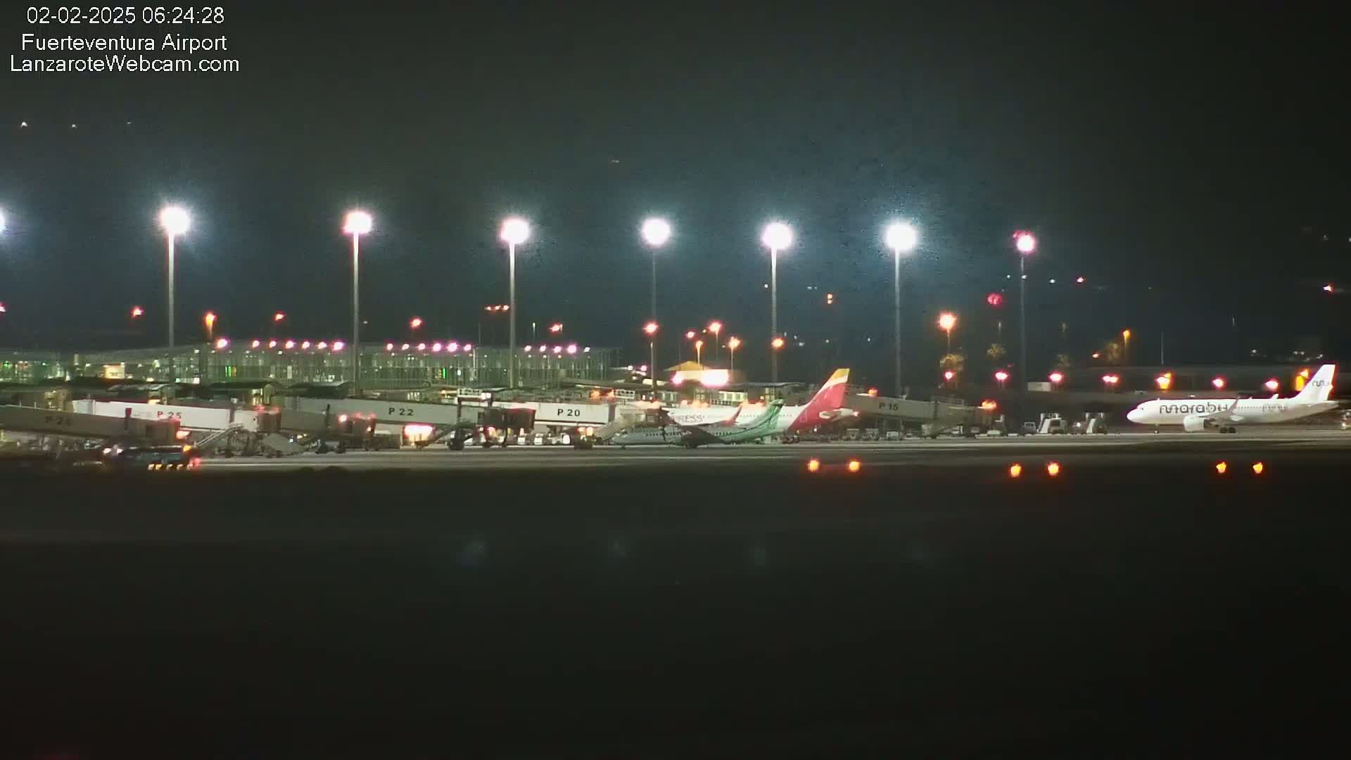 At night, several airplanes are parked at an airport terminal under bright lights.