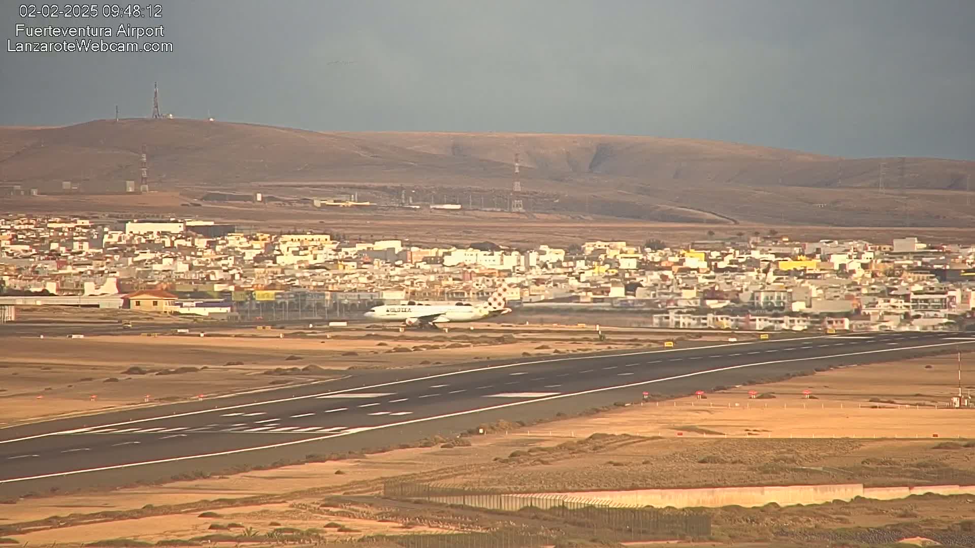 A large passenger airplane taxis on a runway near a town under overcast skies.