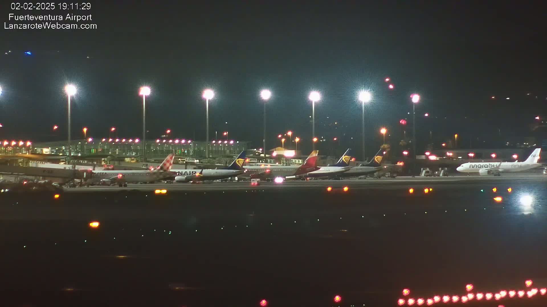 Several airplanes are parked on a tarmac at night under bright lights.