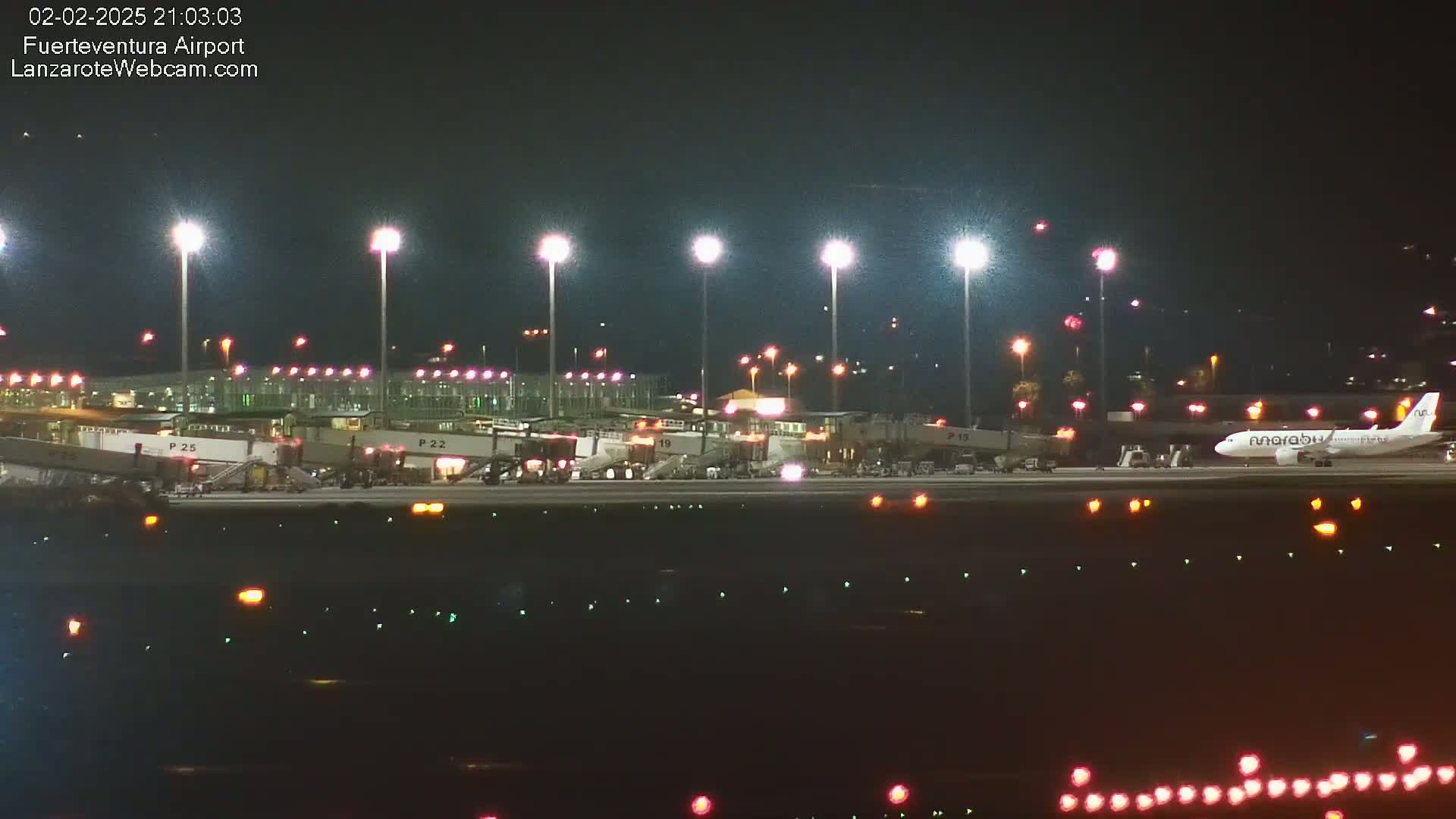 A nighttime view of an airport tarmac with several airplanes parked at gates under bright lights.