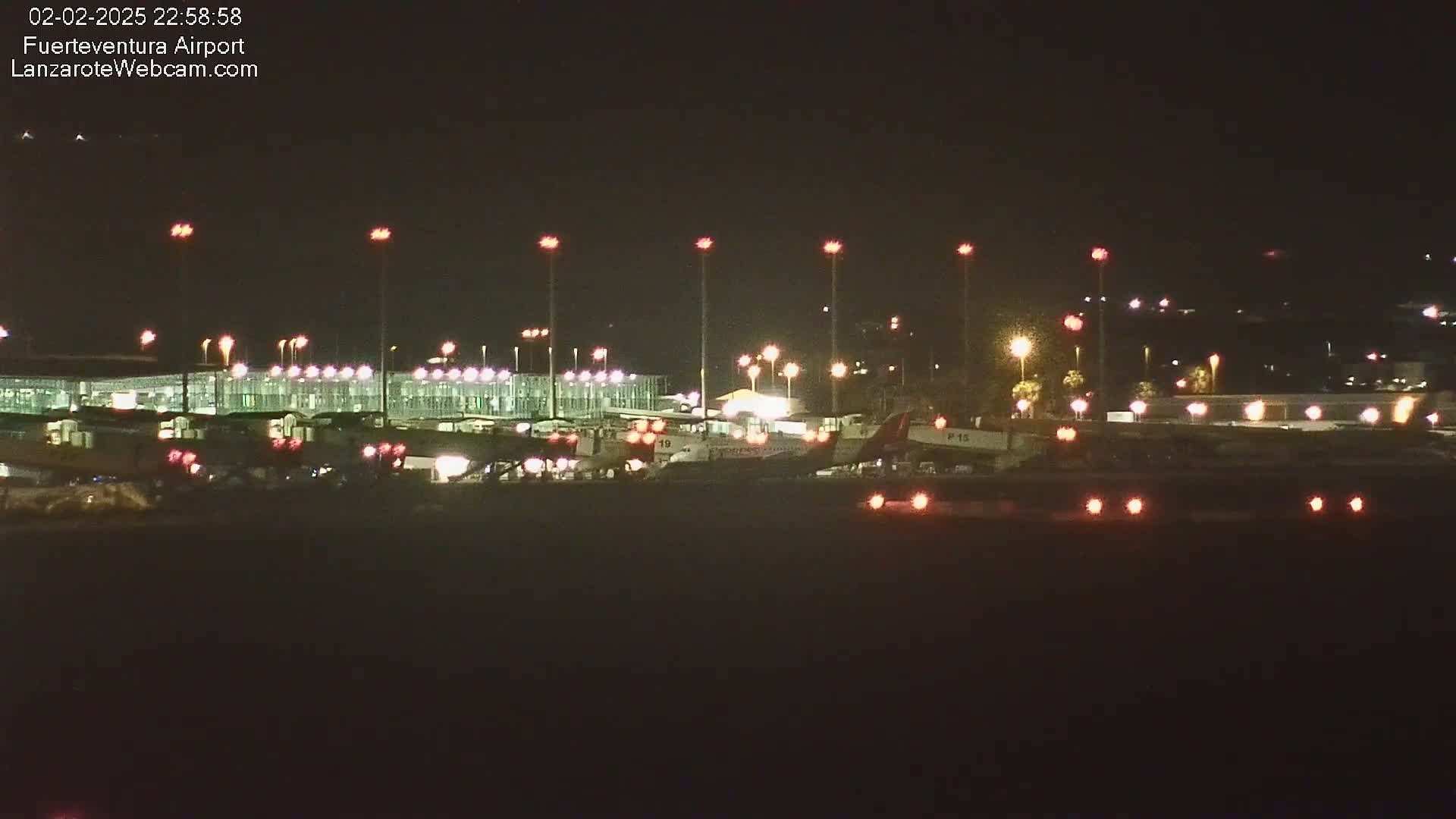 At night, airplanes are parked at a brightly lit airport terminal under a clear, dark sky.