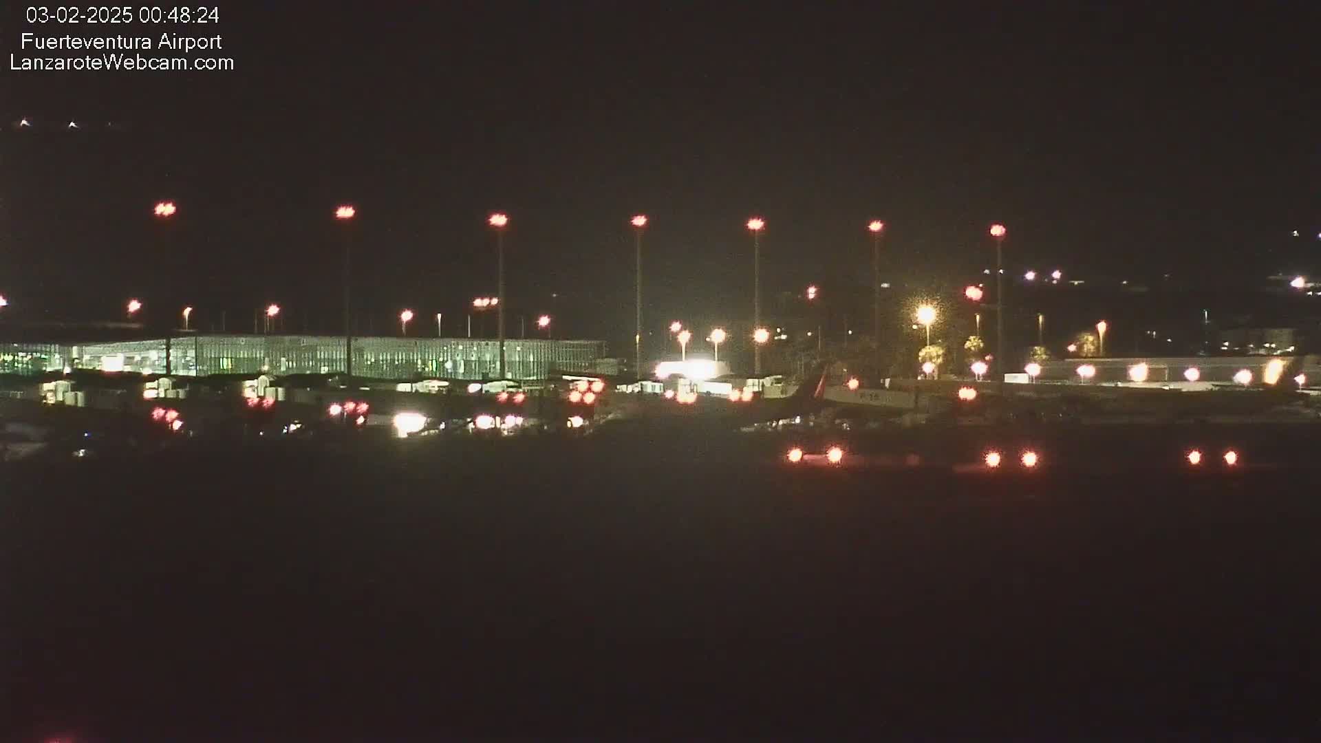 A brightly lit airport at night is seen with several planes and vehicles visible on the tarmac.