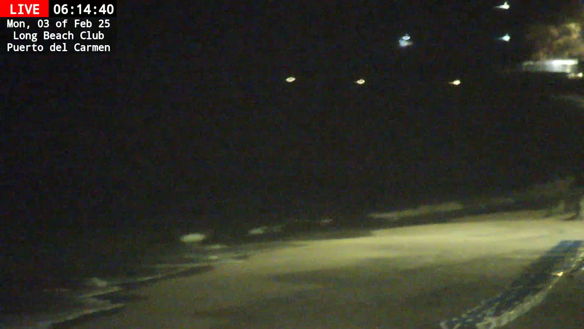 A nighttime, dimly lit beach scene shows a dark body of water and a mostly empty shoreline.