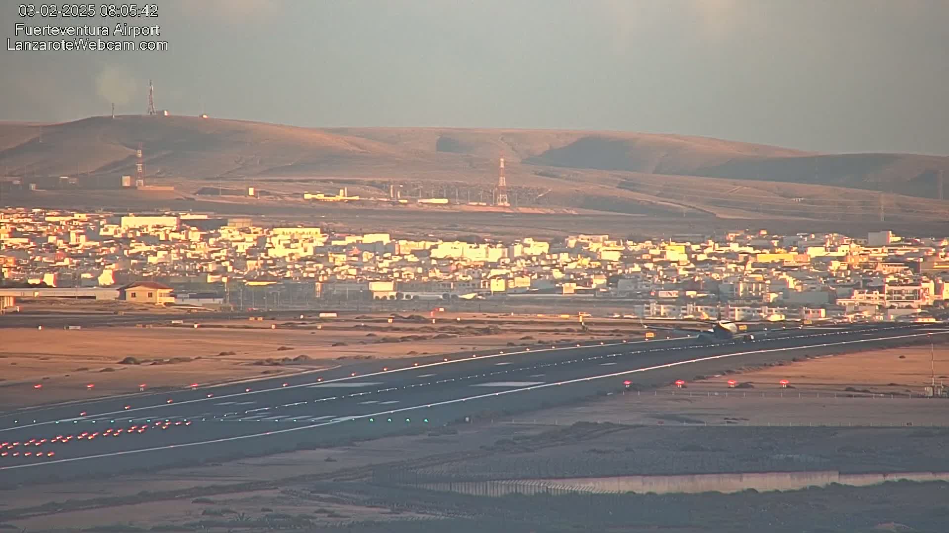 A plane taxis on a runway at an airport near a town, under a hazy, light-colored sky.