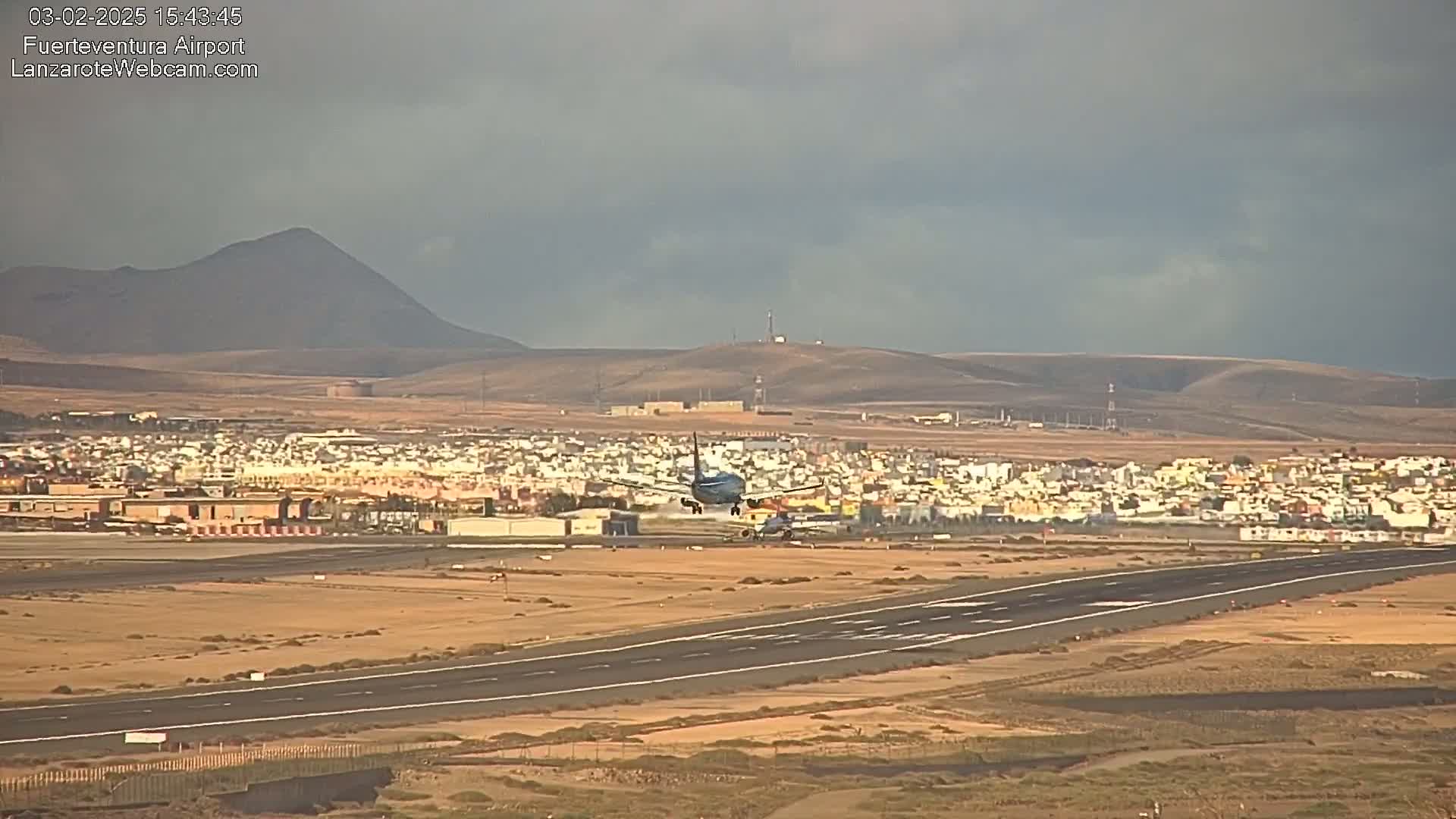 An airplane is landing on a runway at an airport near a town, under an overcast sky.