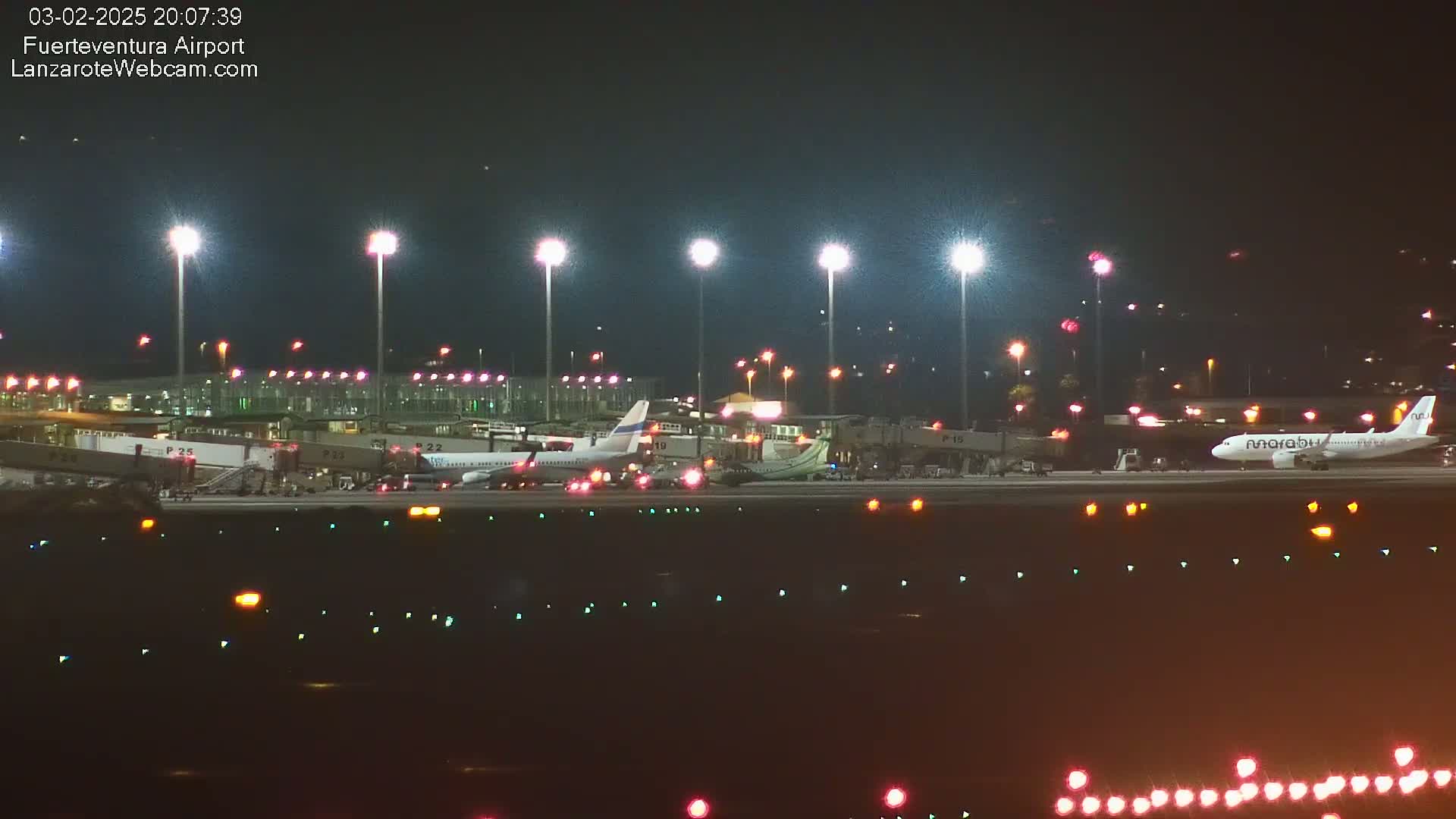 Several airplanes are parked at a brightly lit airport at night.
