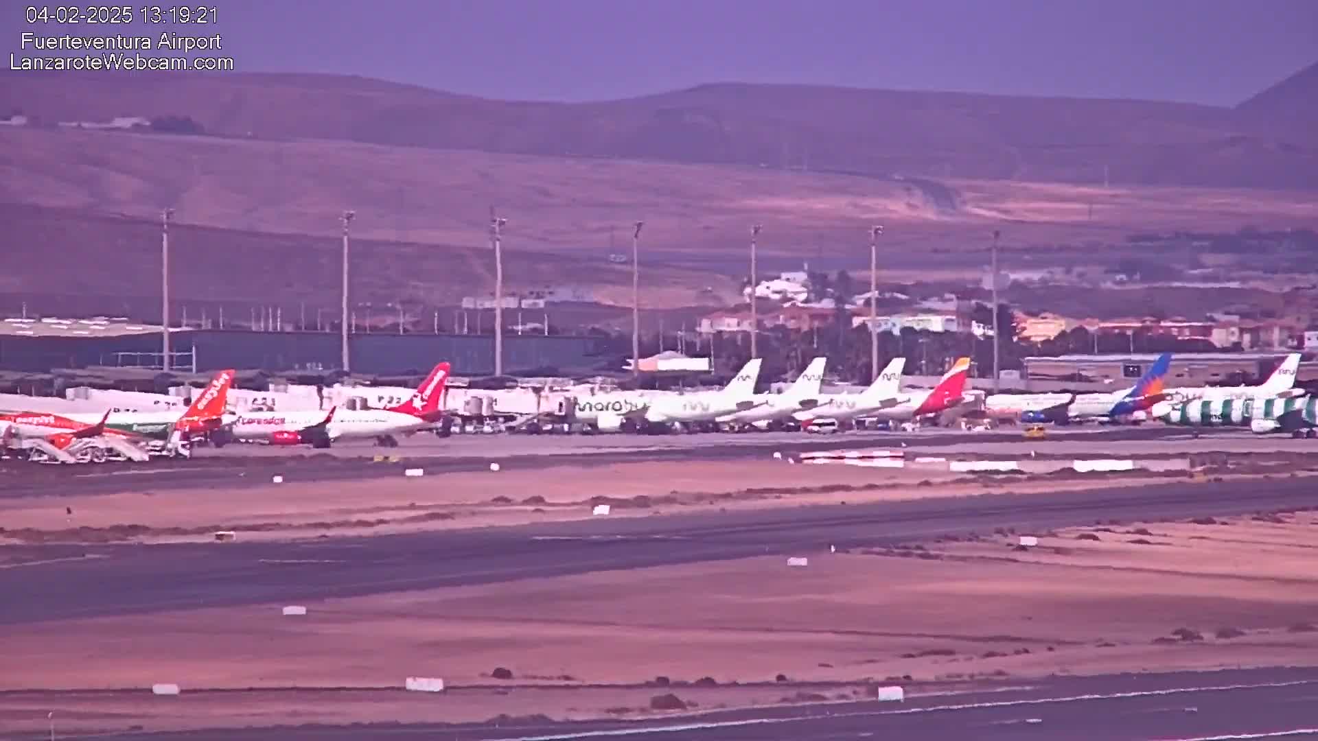 Several airplanes are parked on an airport tarmac under a hazy, light-purple sky.