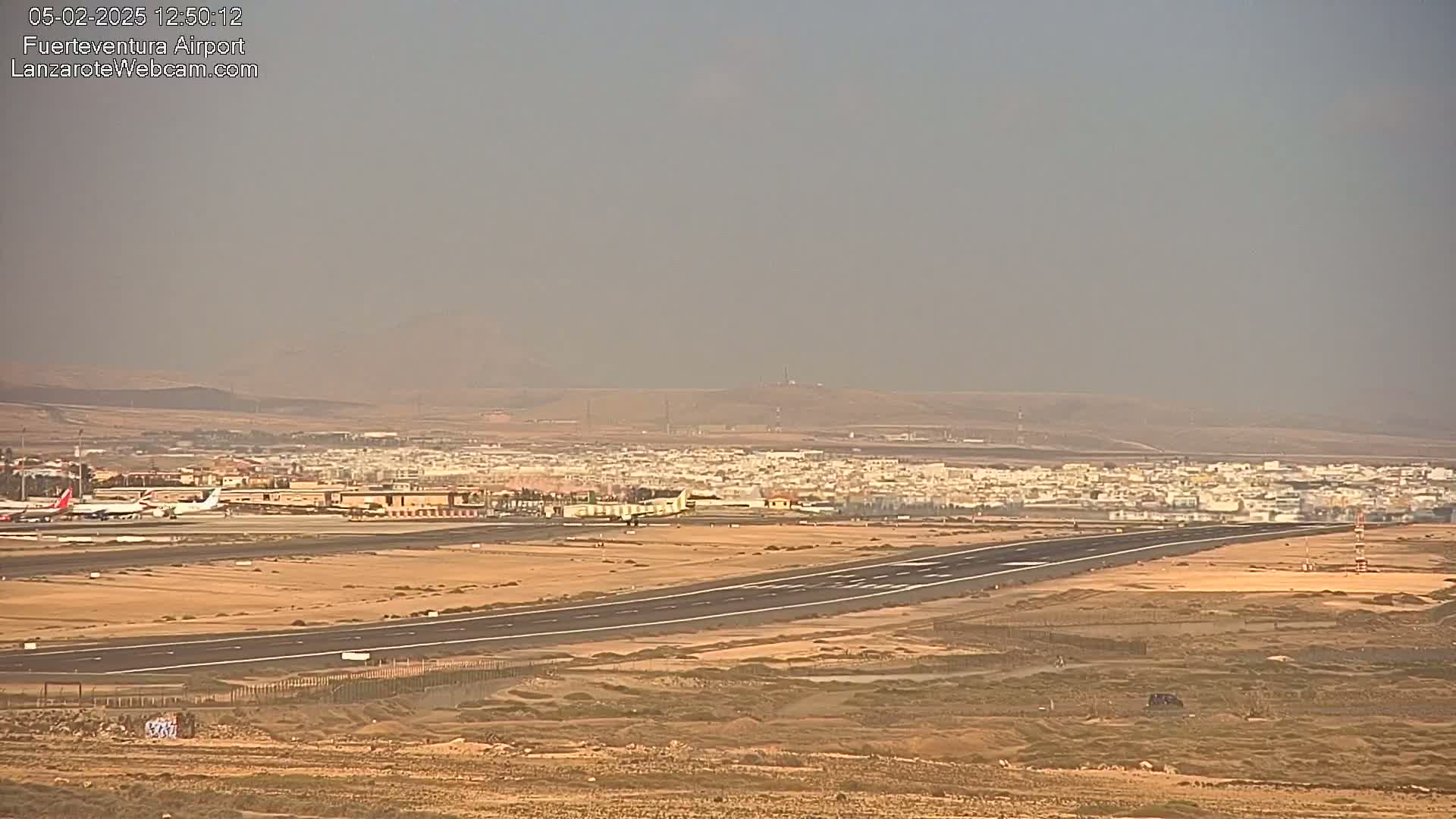 A hazy view of an airport runway with several planes, surrounded by a town and arid landscape.