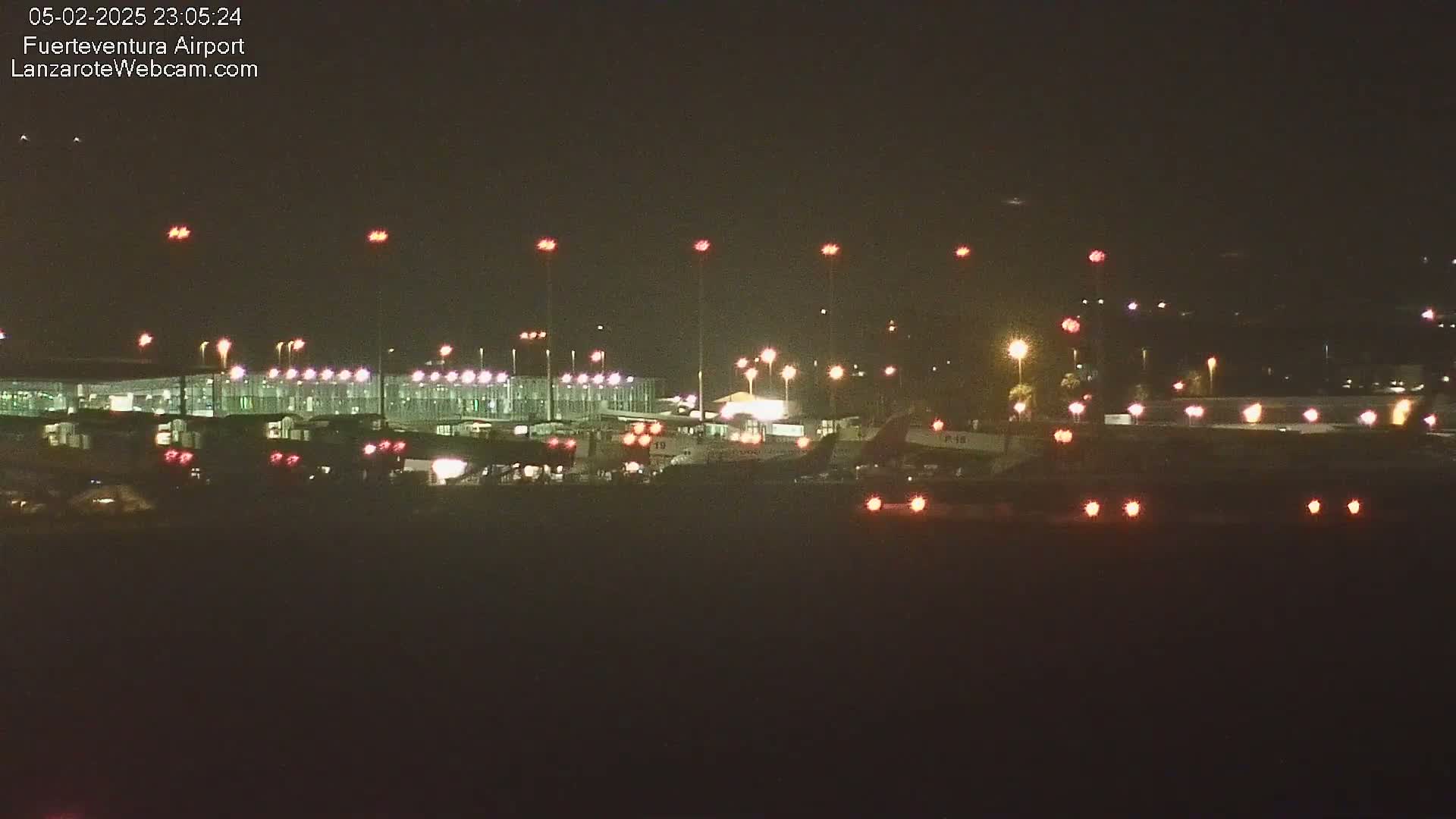 A nighttime view of an airport terminal and airplanes on the tarmac, illuminated by numerous lights.