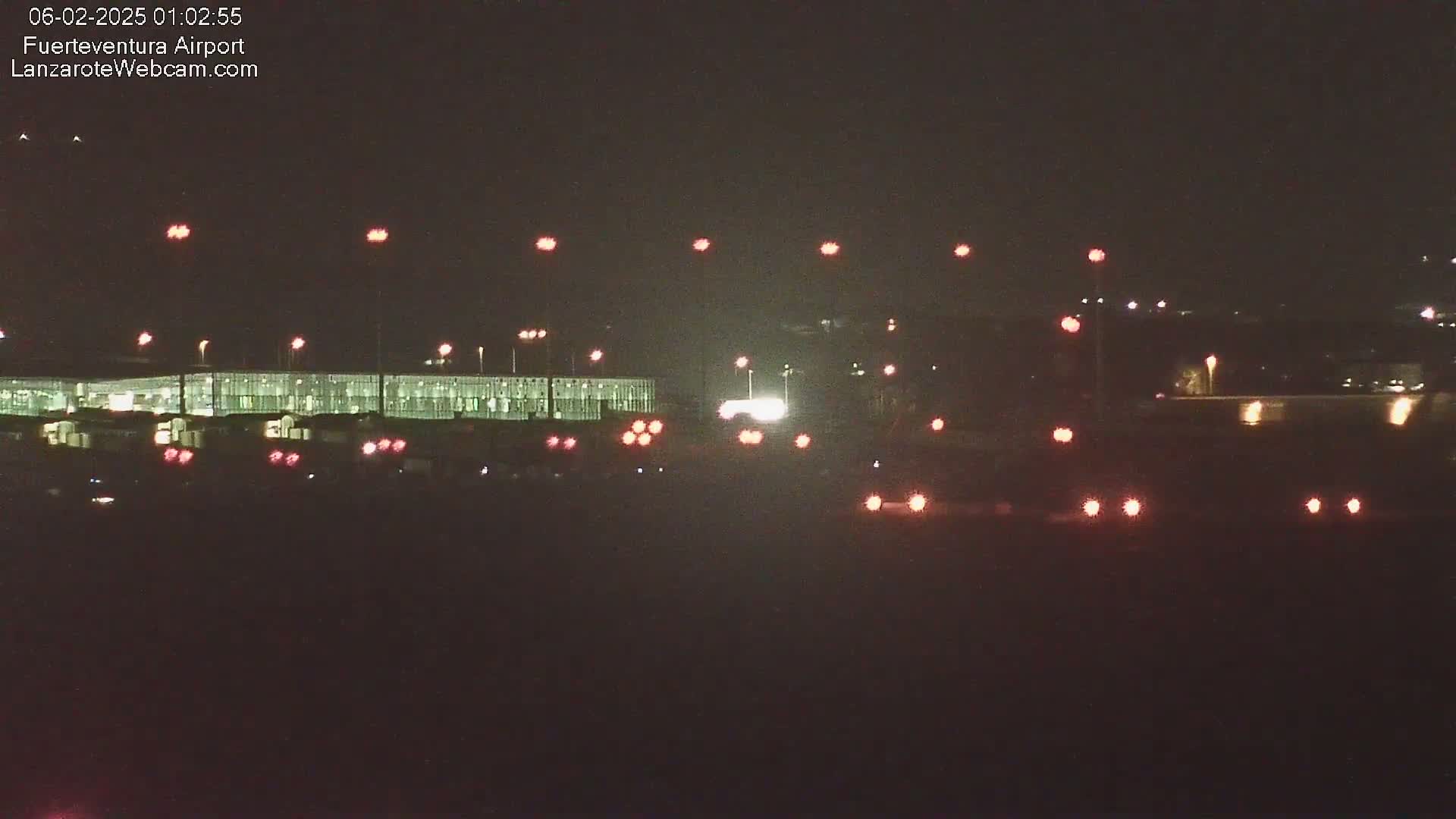 A nighttime view of an airport terminal building and runway lights under a dark sky.