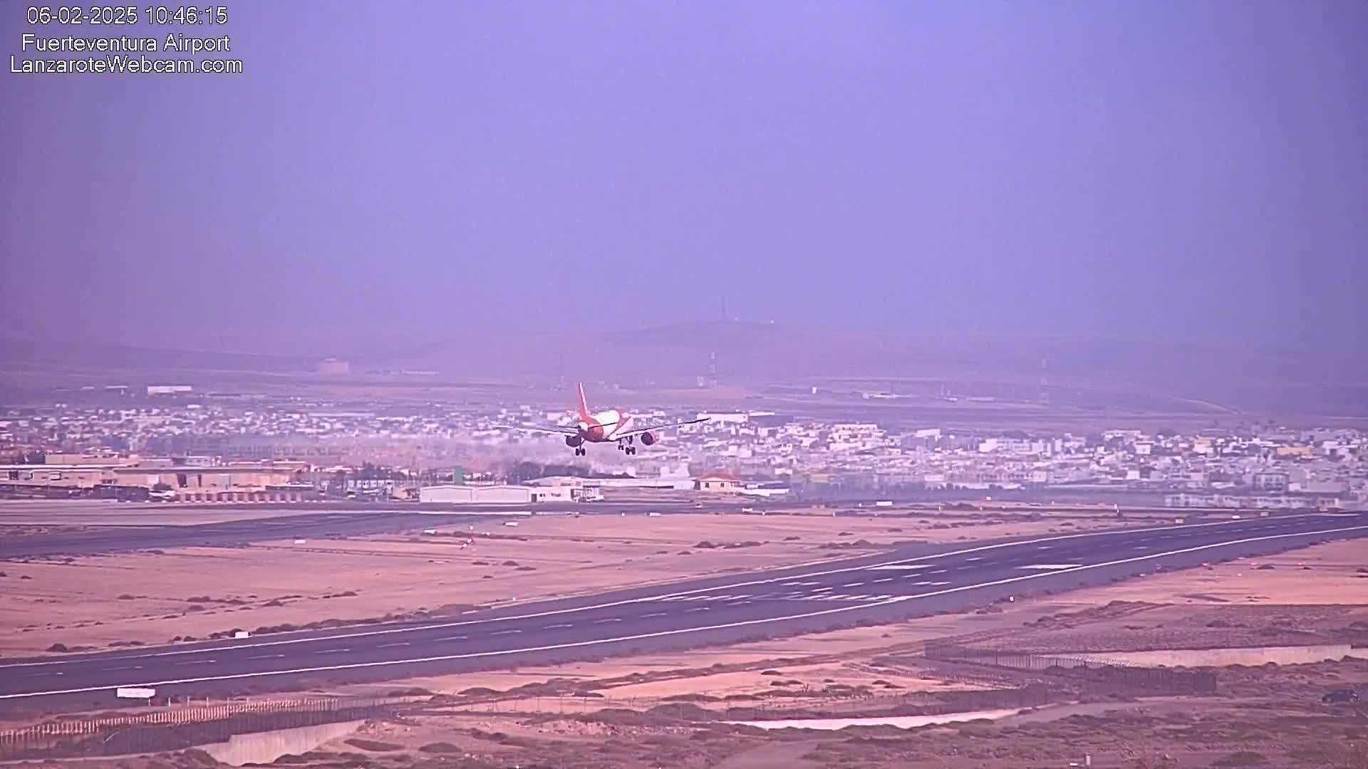 A plane is landing on a runway at an airport on a hazy day.