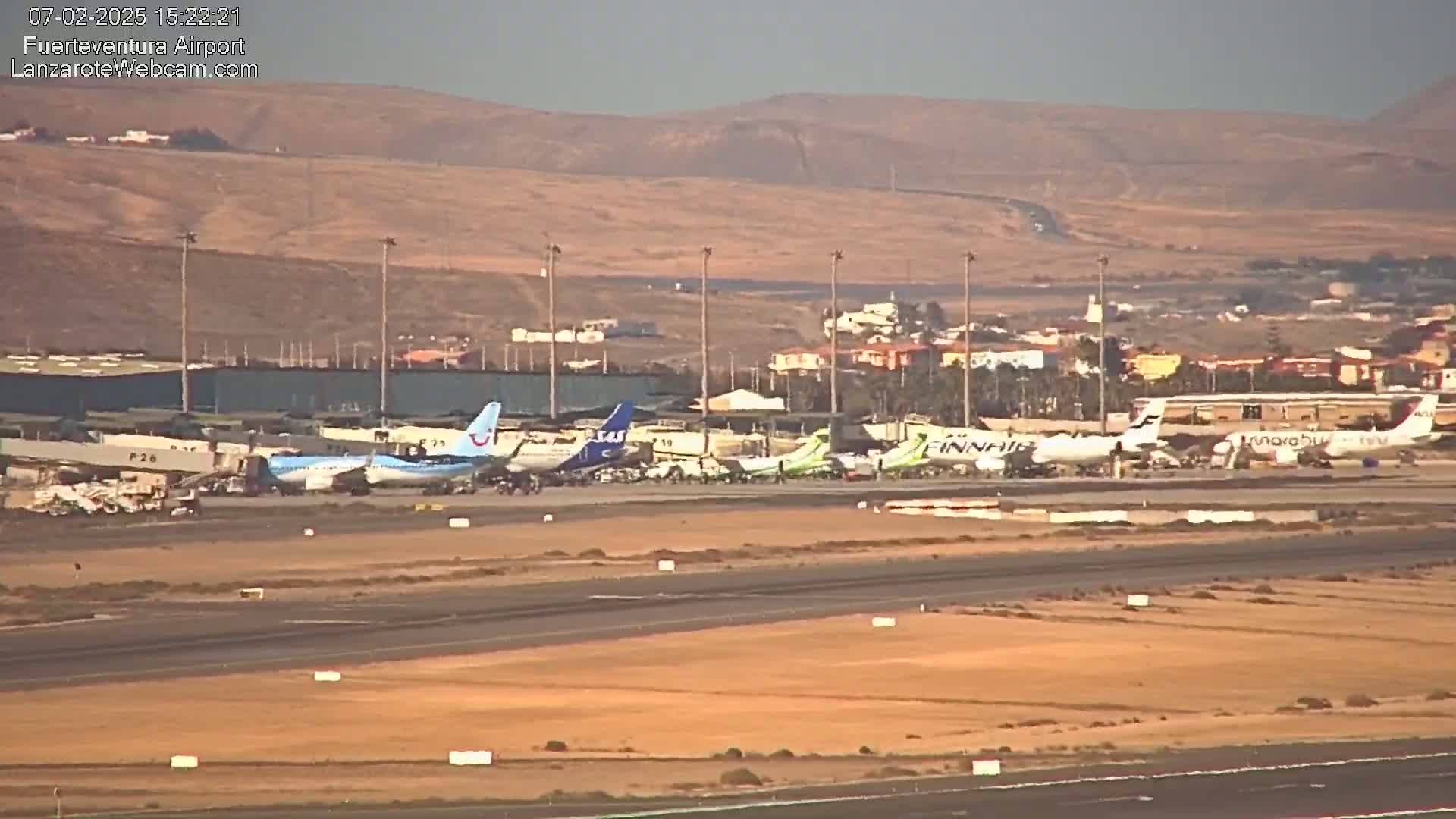 Several airplanes are parked on an airport tarmac under hazy conditions with tan-colored hills in the background.