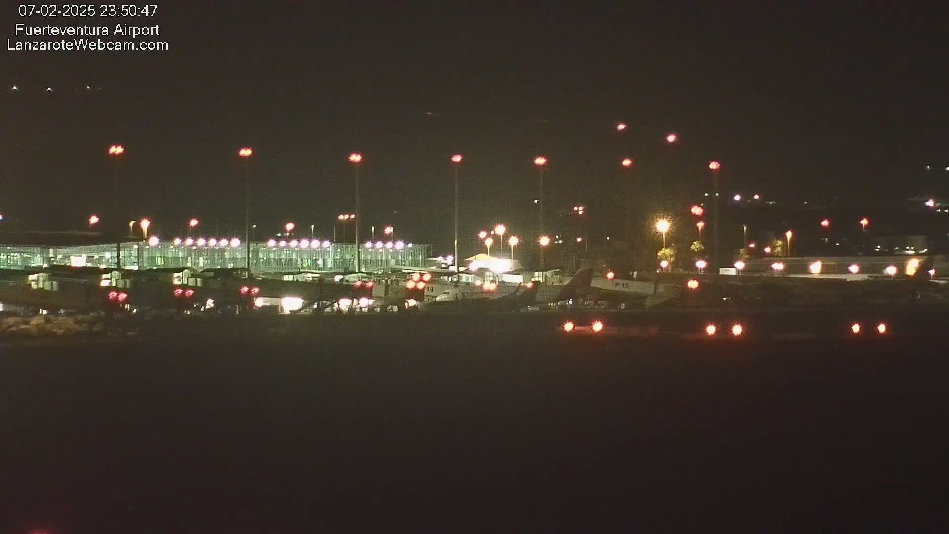 At night, several airplanes are parked at a brightly lit airport terminal under a clear, dark sky.