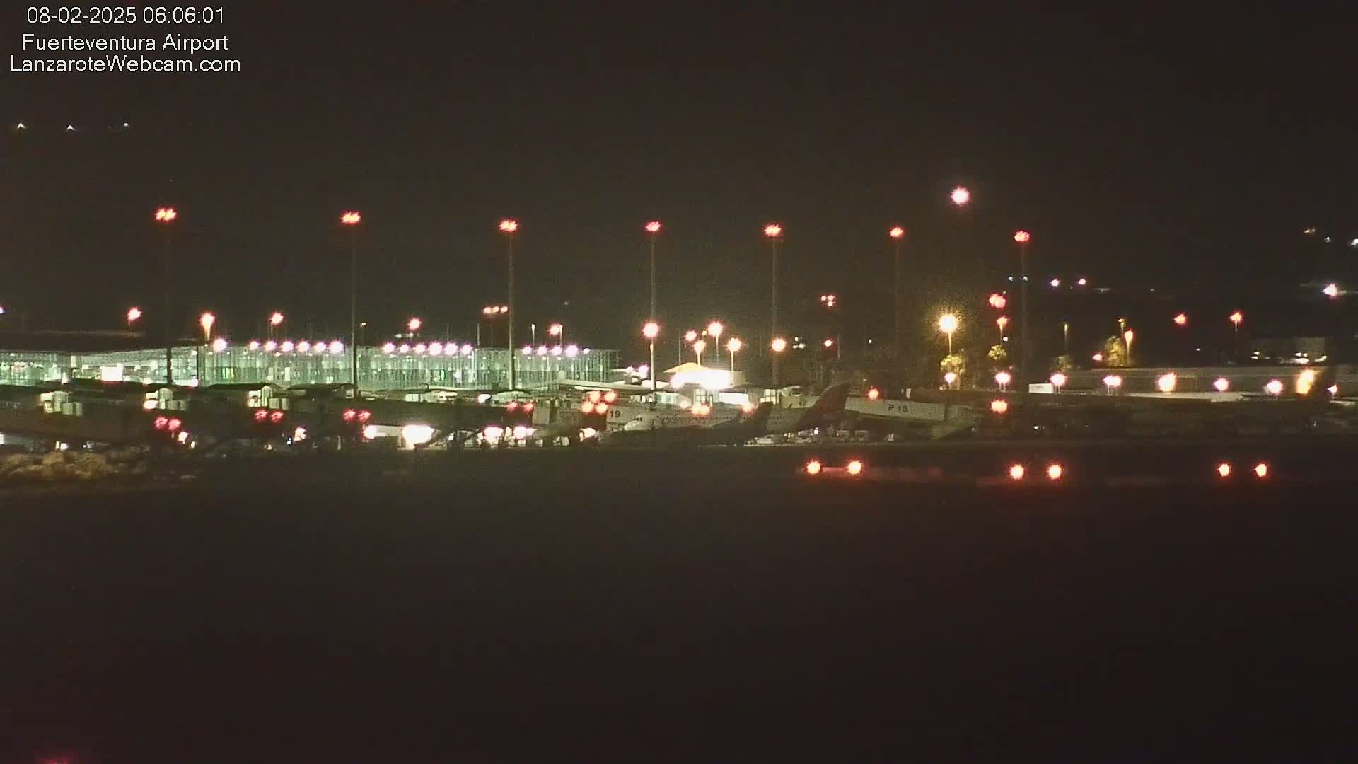 At night, brightly lit airplanes are parked at a terminal building at an airport under a clear, dark sky.