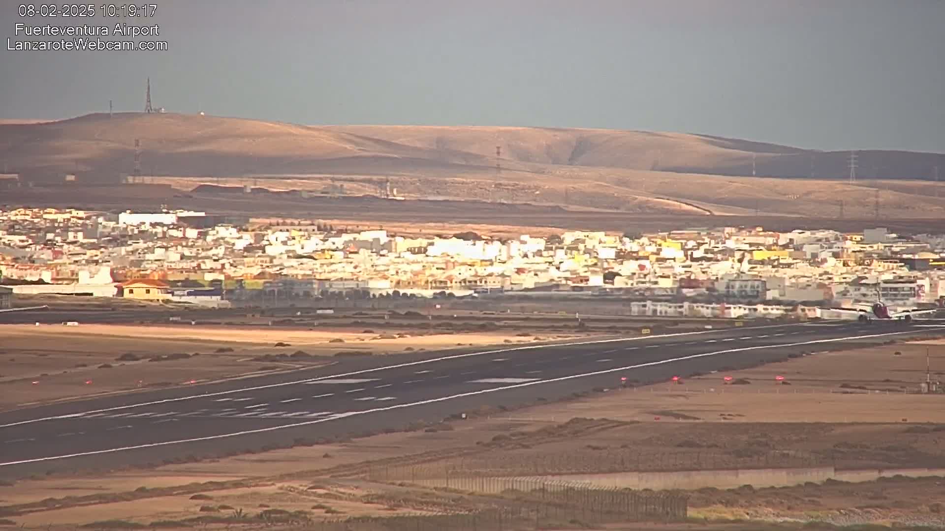 An airplane is landing on a runway near a town under a partly cloudy sky.