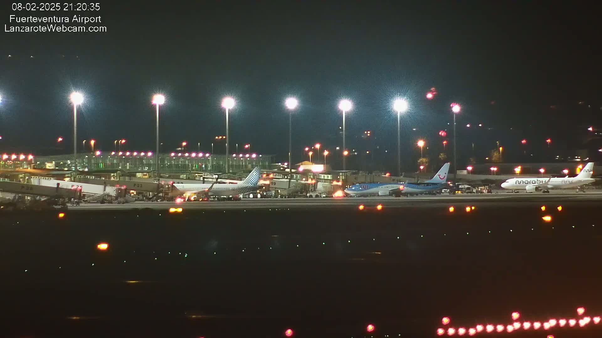 At night, several airplanes are parked at an airport terminal under bright lights.
