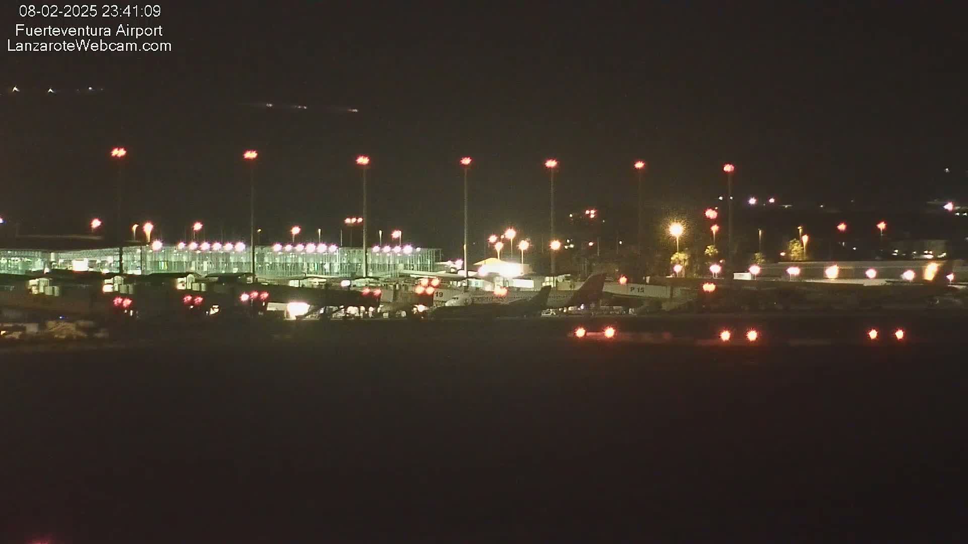 At night, an airport terminal and several airplanes are illuminated by bright lights.