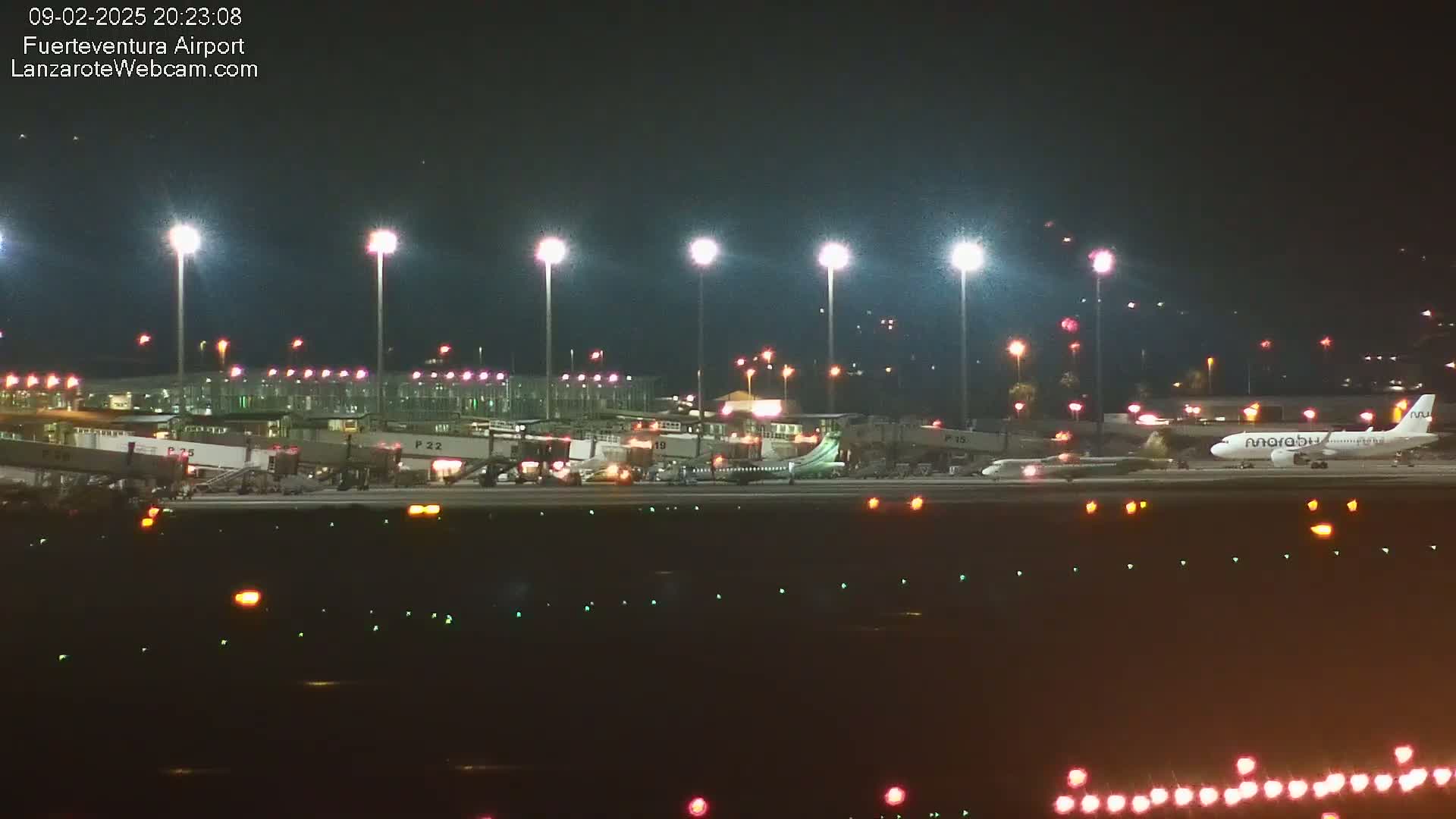 A brightly lit airport at night shows several airplanes at gates and on the tarmac.