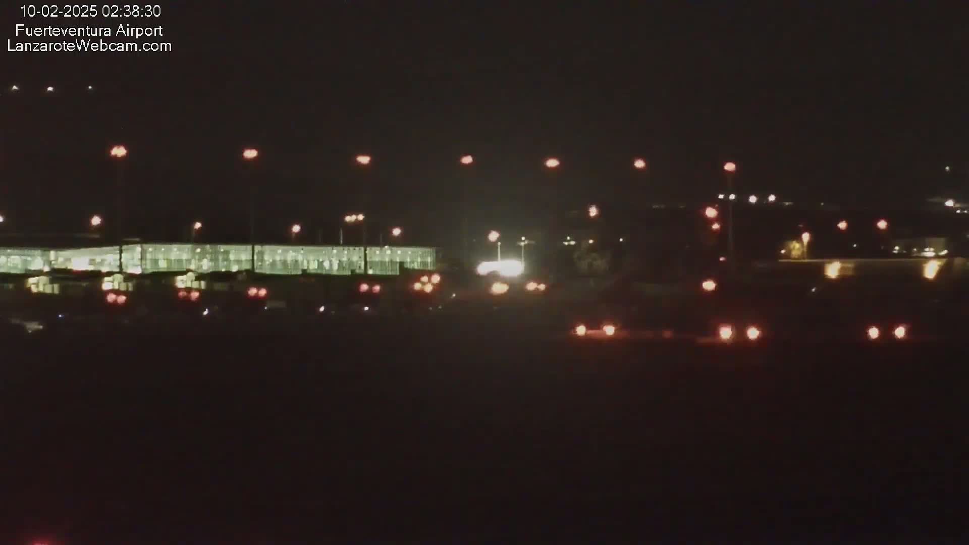 A nighttime view of an airport terminal building with numerous lights illuminating the surrounding area and vehicles.