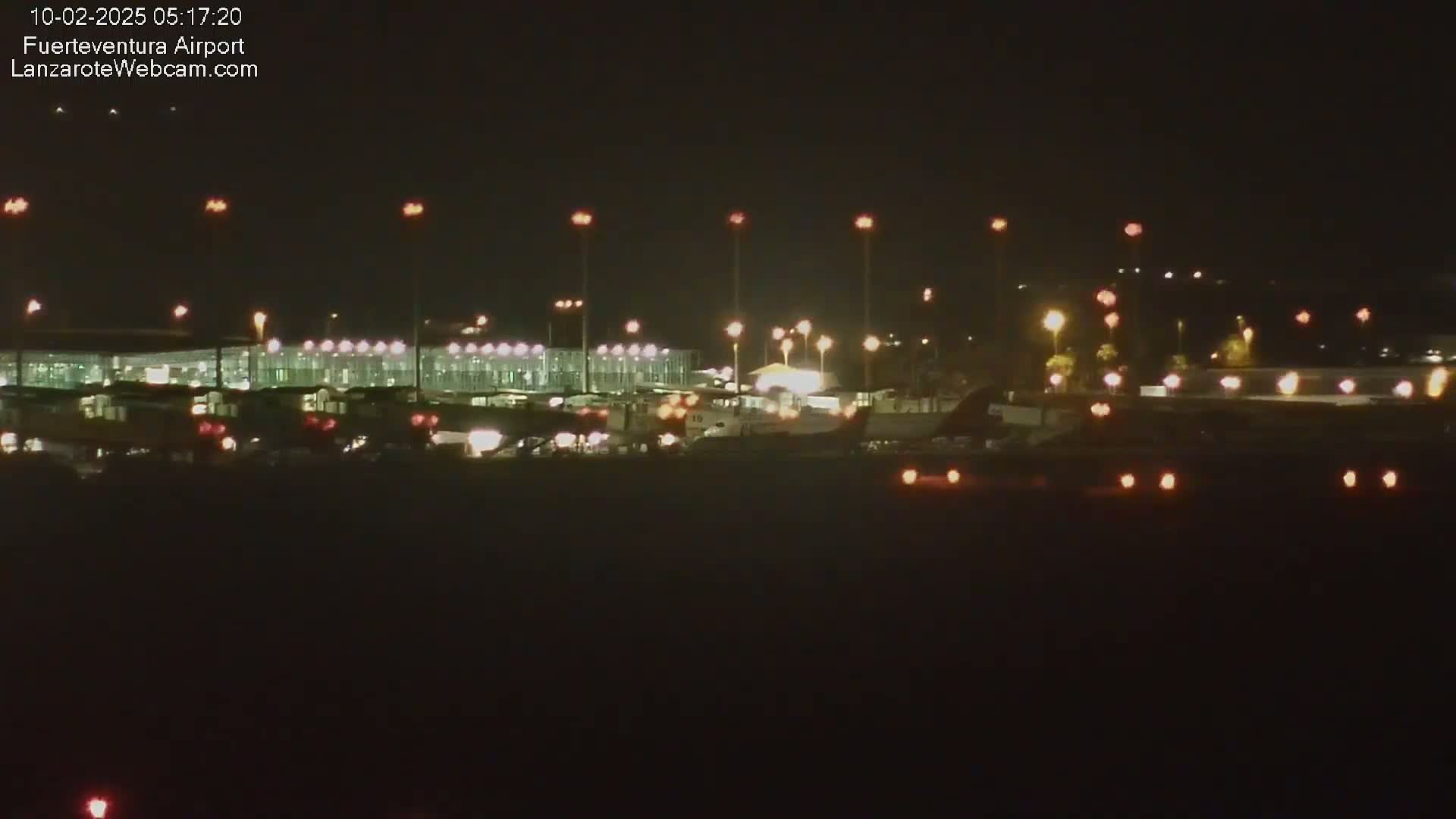 A brightly lit airport at night is shown, with planes and vehicles visible on the tarmac.