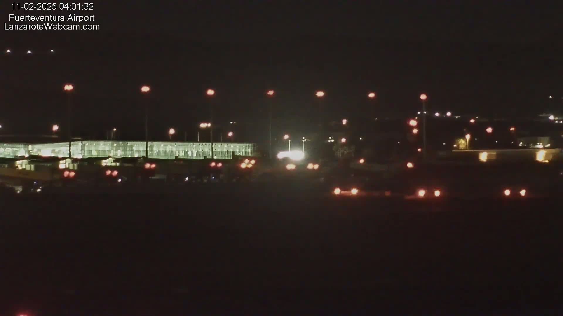 A nighttime view of an airport terminal with numerous lights illuminating the tarmac and surrounding area under a clear, dark sky.