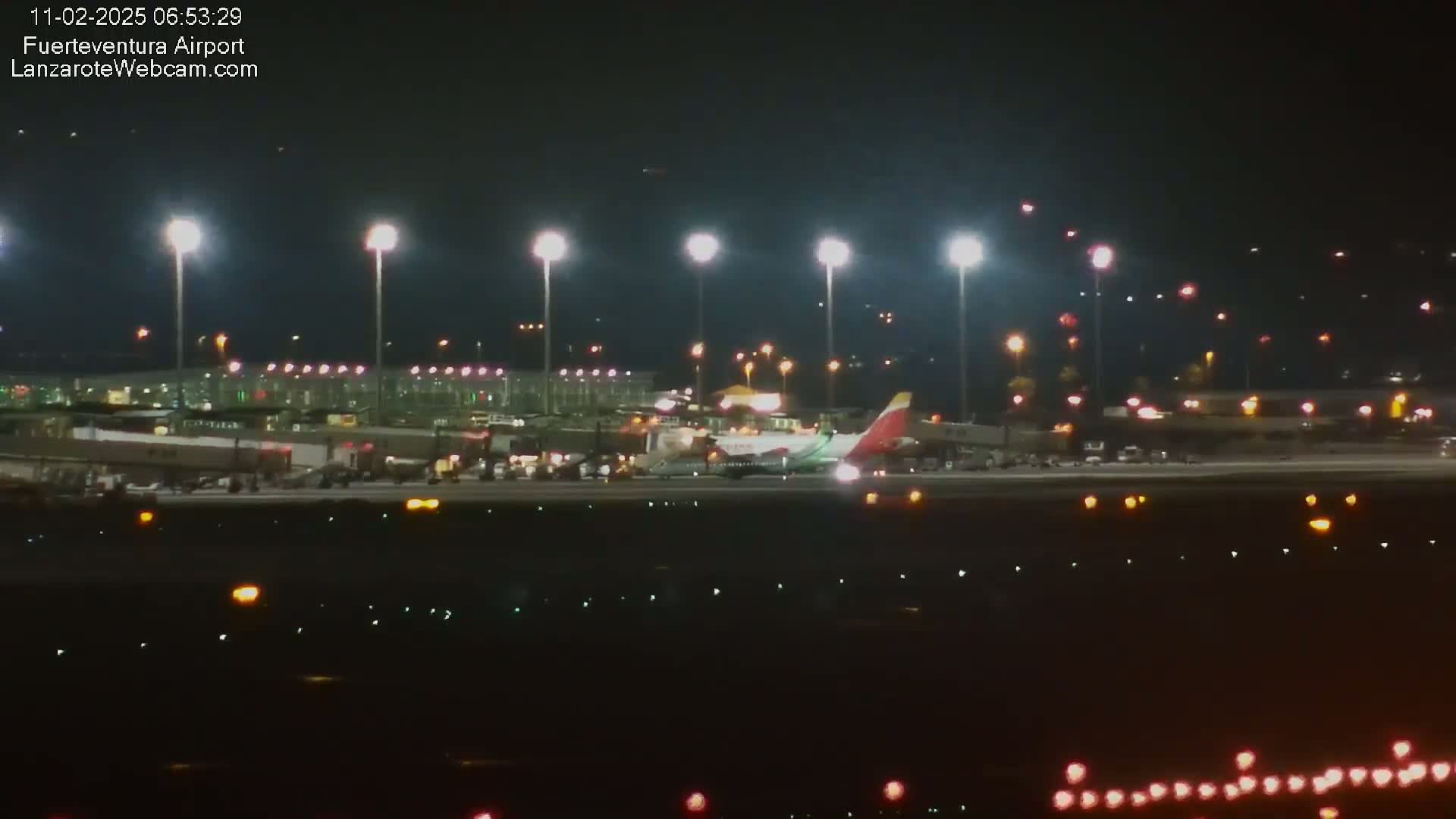 At night, an airplane is parked on an airport tarmac illuminated by bright lights.