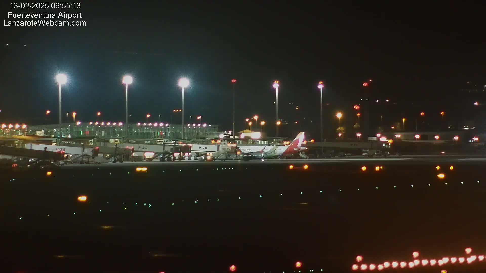 At night, several airplanes are parked at gates at an airport under bright lights.