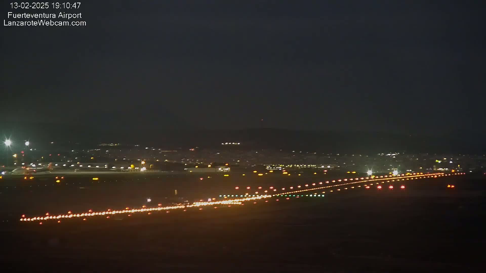 A nighttime long shot of an airport runway illuminated with lights, against a dark sky.