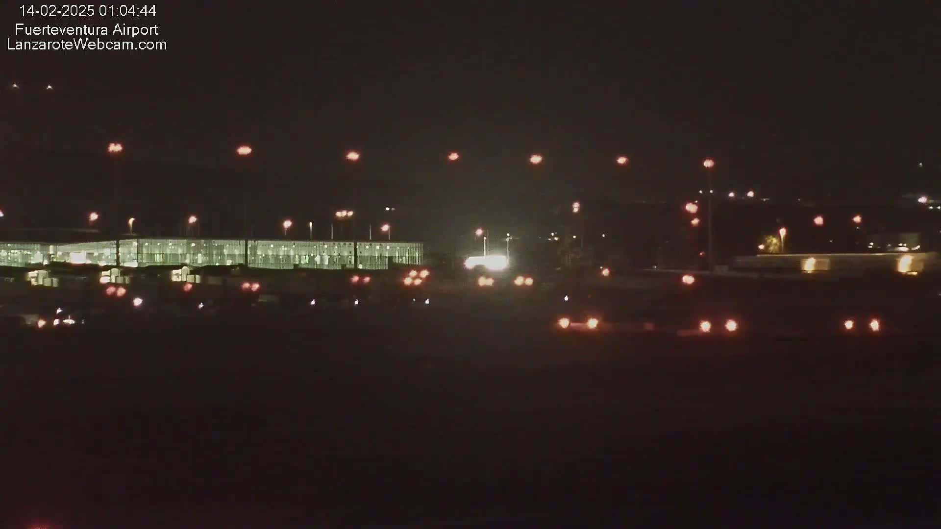 A nighttime view of an airport terminal building with numerous lights illuminating vehicles and the surrounding area under a clear, dark sky.