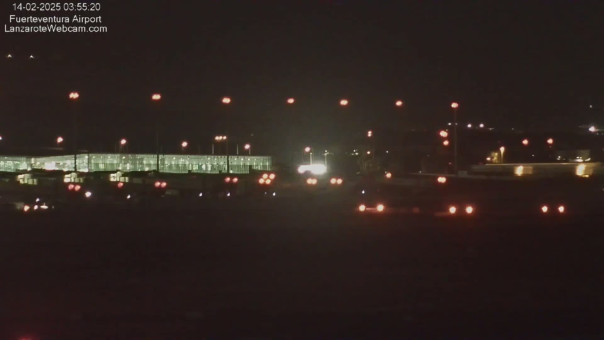 A nighttime view of an airport terminal building and roadway with vehicle lights visible.