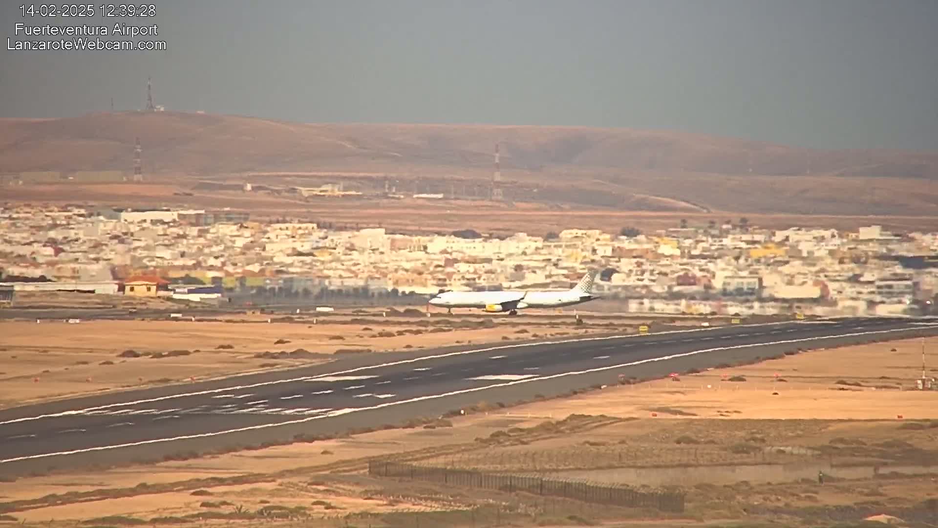 A passenger airplane is landing on a runway near a town under hazy conditions.