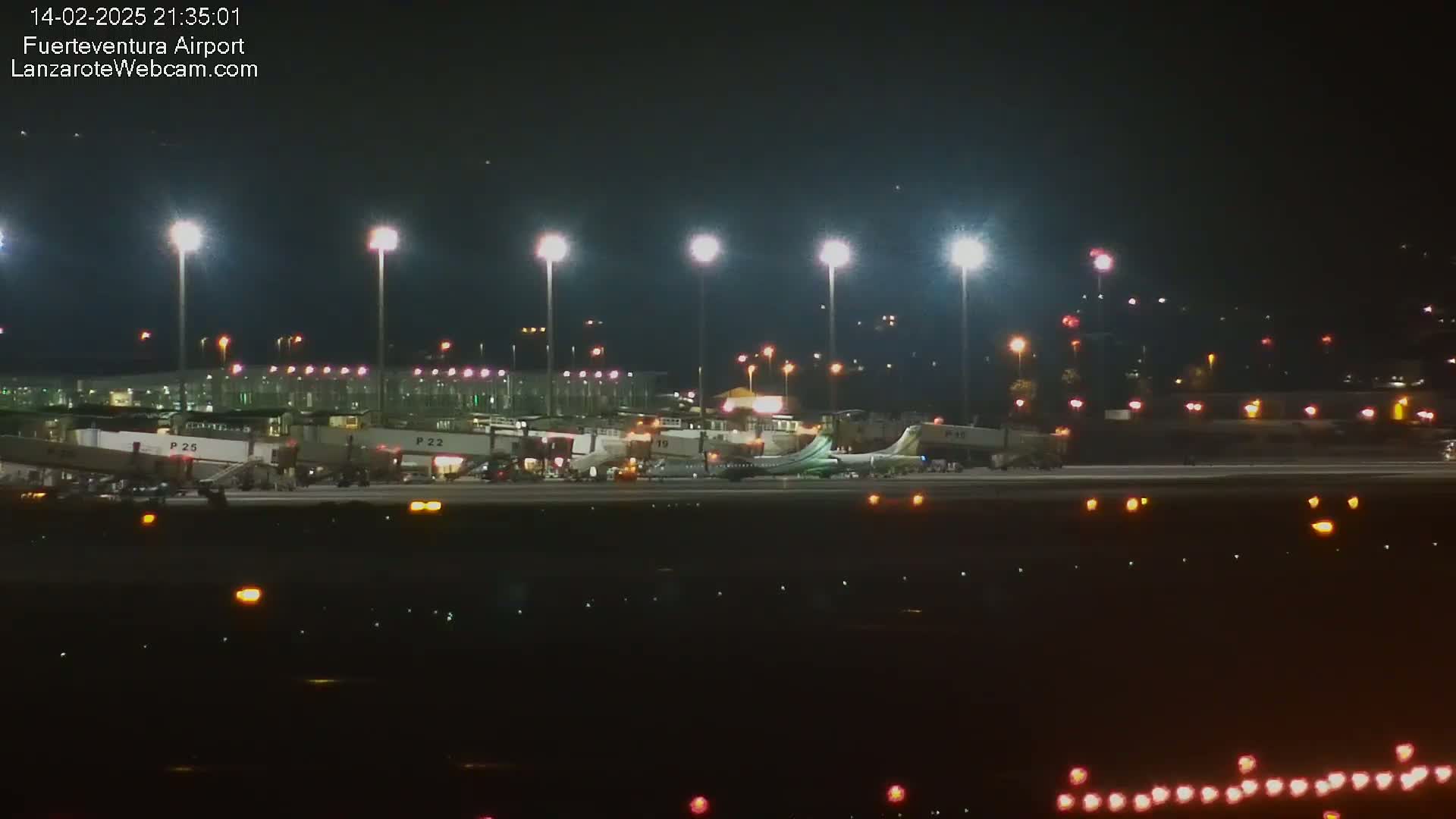 A plane sits on the tarmac of a brightly lit airport at night.