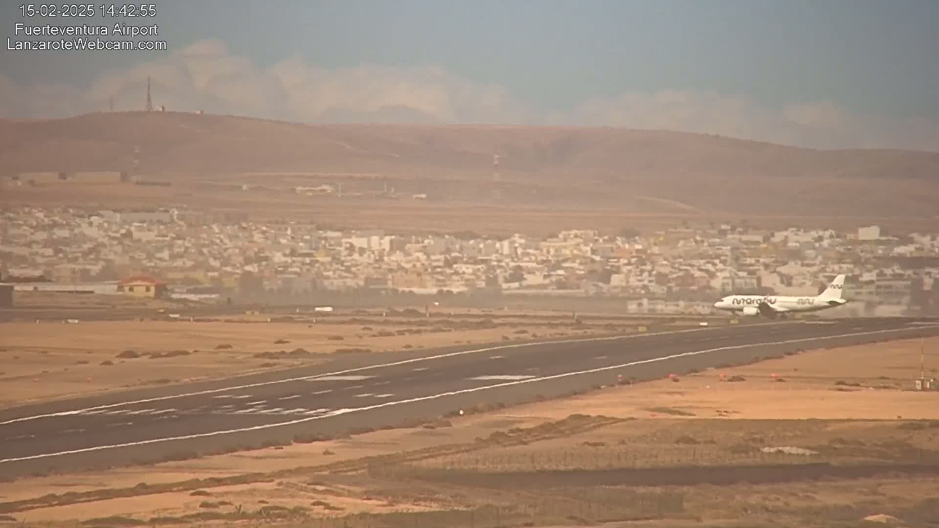 A plane is landing on a runway near a town in hazy conditions.