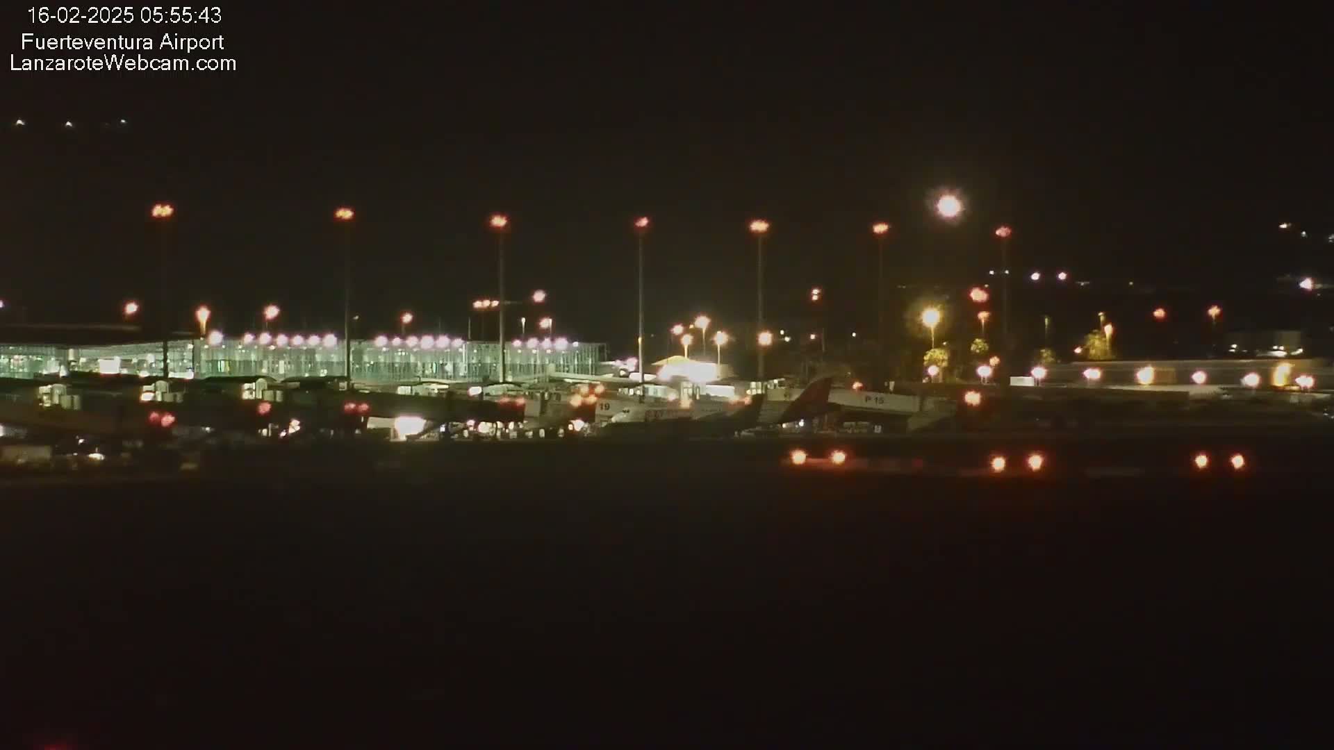 At night, several airplanes are parked at a brightly lit airport.