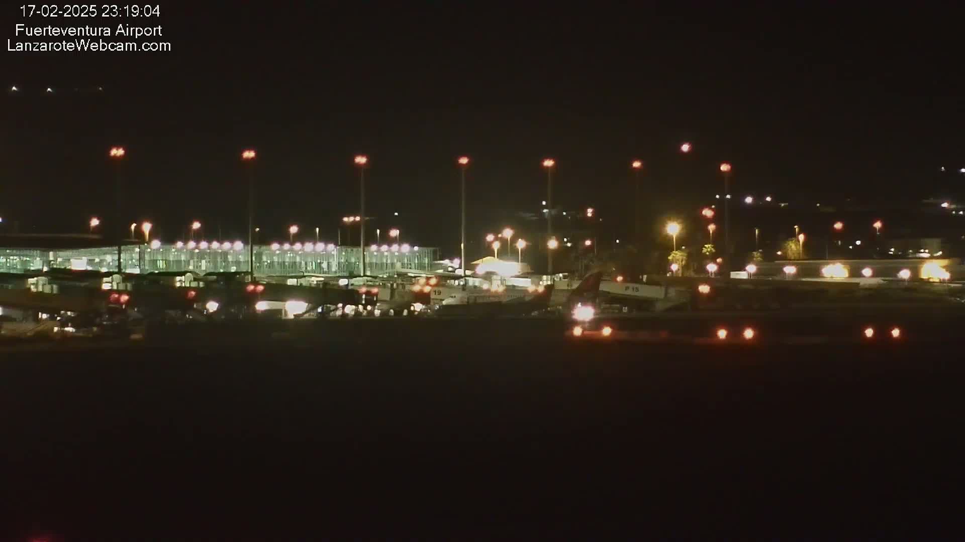 A nighttime view of an airport terminal and tarmac with several airplanes visible under clear skies.