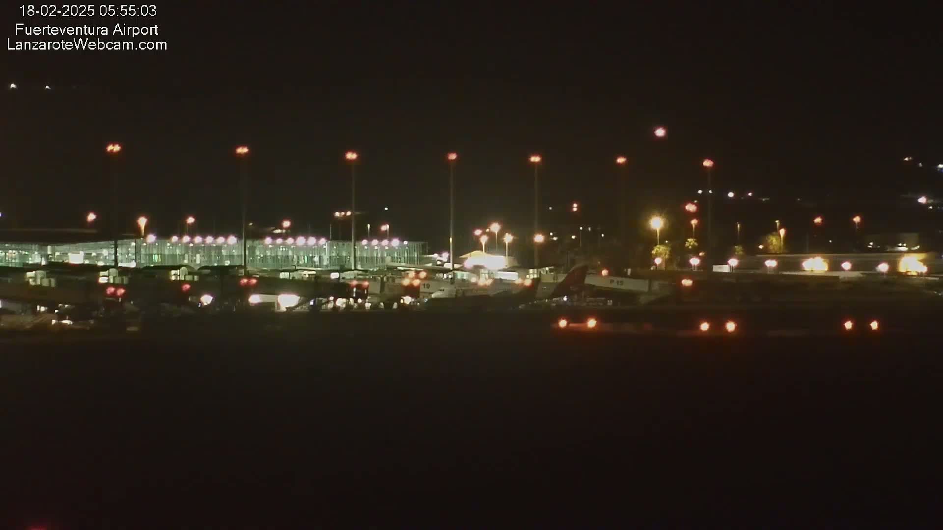 At night, a brightly lit airport terminal and several airplanes are visible on the tarmac.