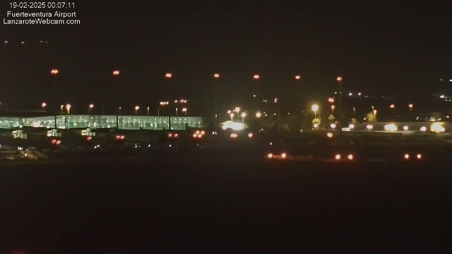 A brightly lit airport terminal and surrounding area are visible at night.