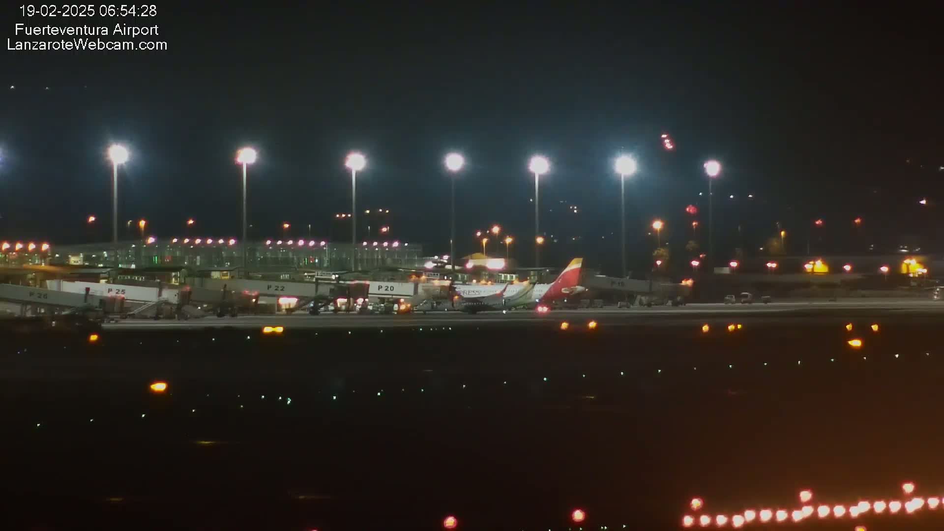 A passenger airplane is parked at a brightly lit airport at night.