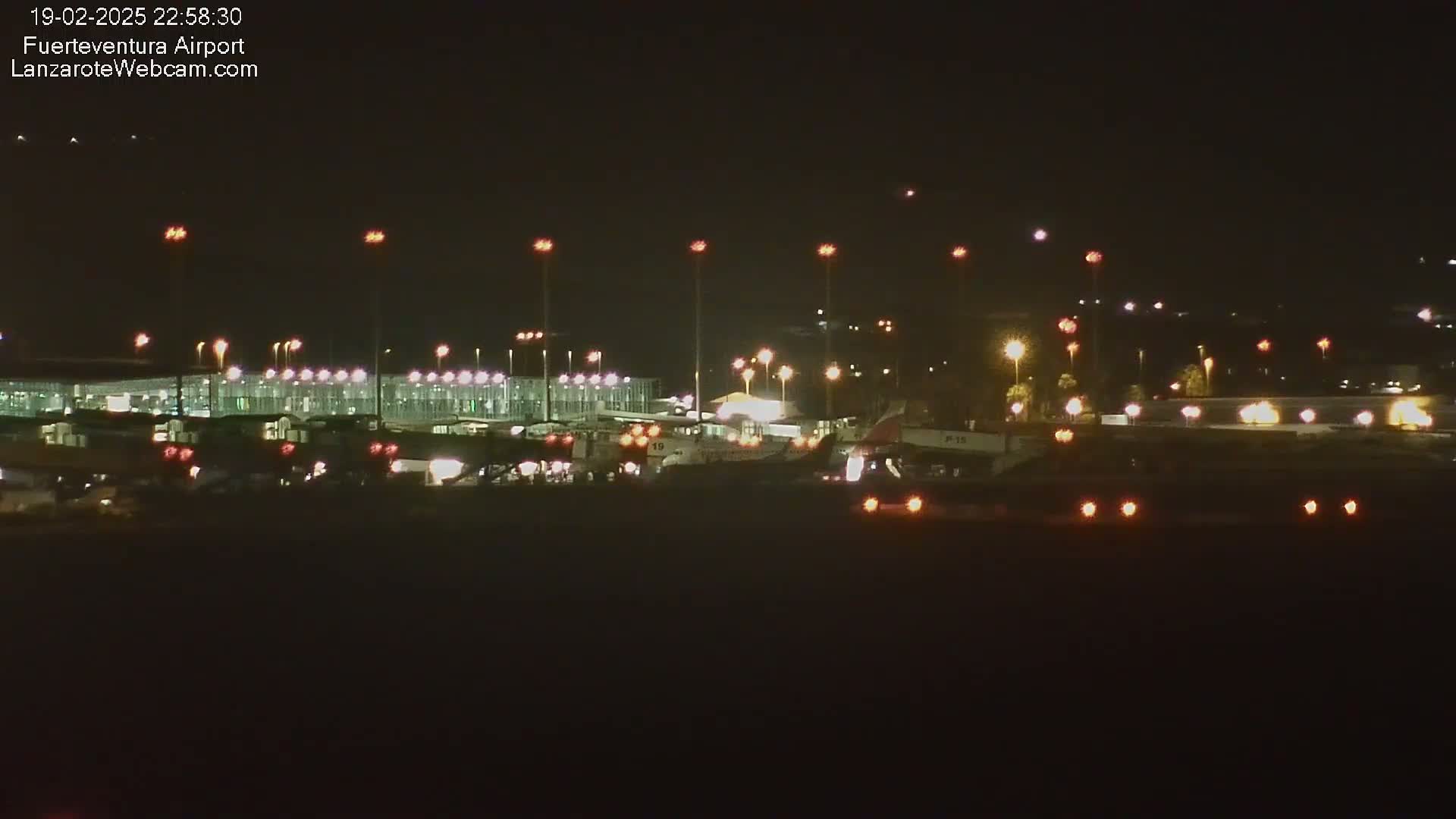 A nighttime view of an airport terminal and several airplanes on the tarmac under a clear, dark sky.