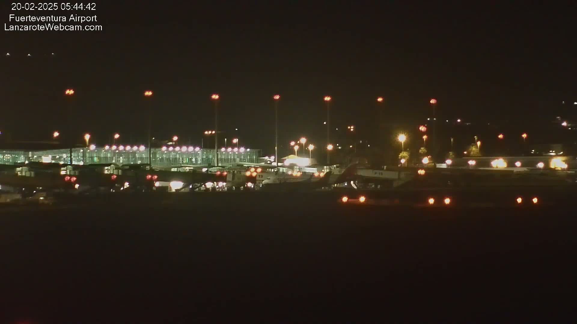 A brightly lit airport terminal and several airplanes are visible at night.