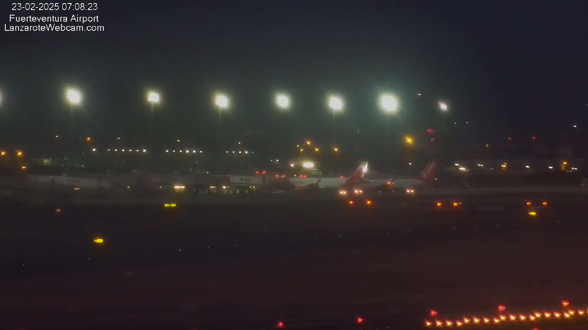 A passenger airplane is parked on an airport tarmac at night under hazy, dimly lit conditions.