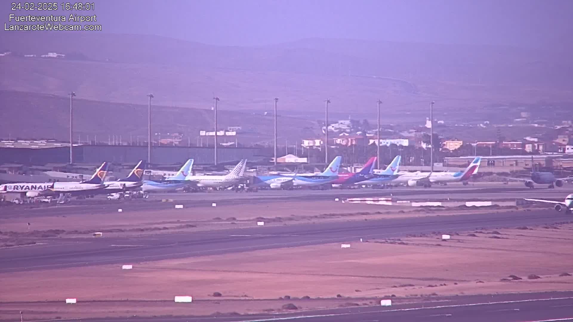 A row of several passenger airplanes is parked on an airport tarmac under hazy conditions.