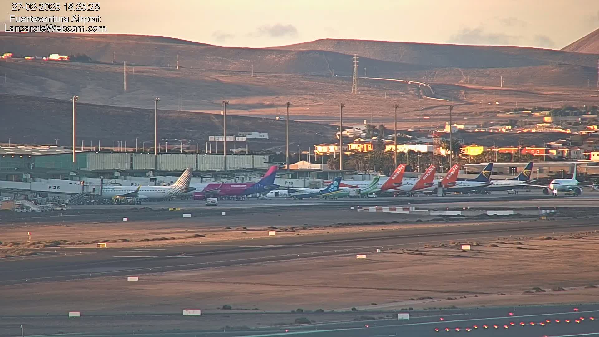 Several airplanes are parked at an airport under a clear, dusky sky near brown hills.